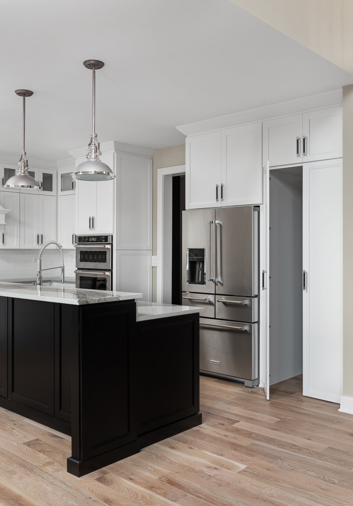 A kitchen with a black island , white cabinets , stainless steel appliances and hardwood floors.