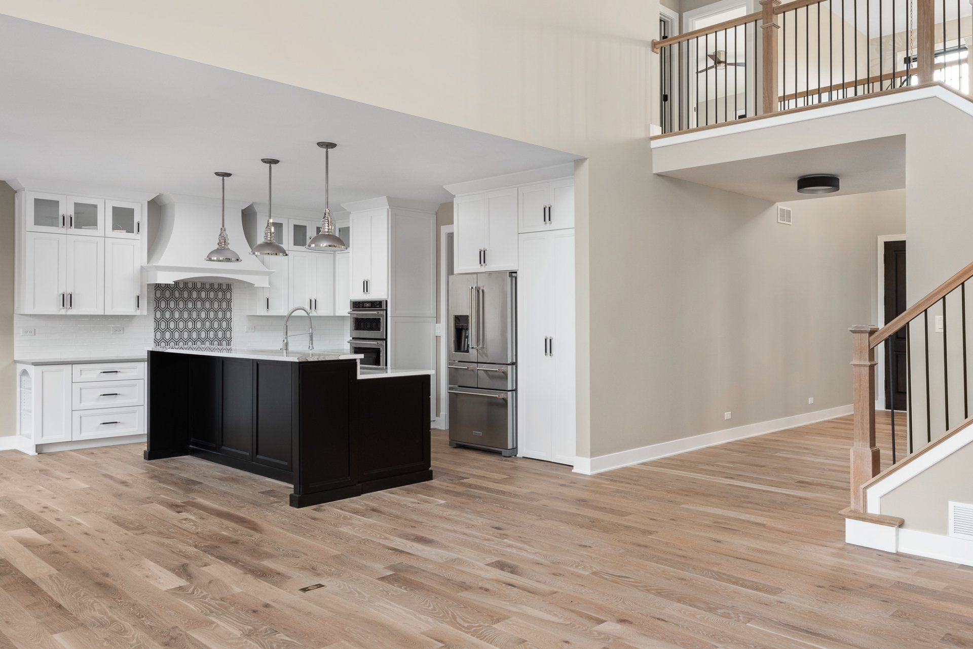 A kitchen with a black island , white cabinets , stainless steel appliances and hardwood floors.