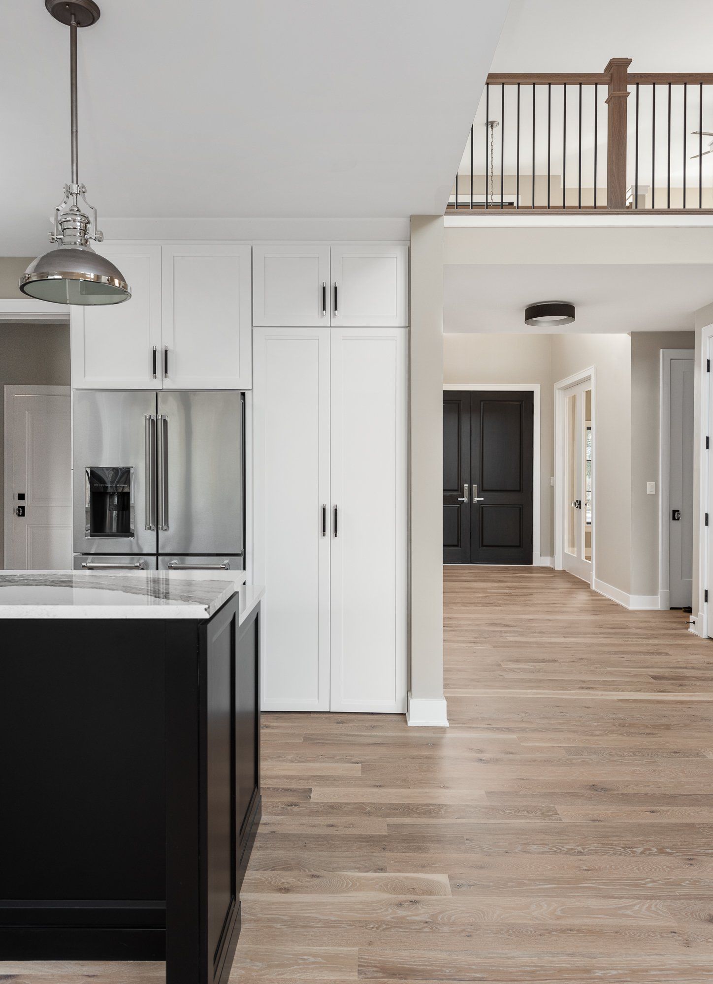A kitchen with a black island , white cabinets , stainless steel appliances and hardwood floors.
