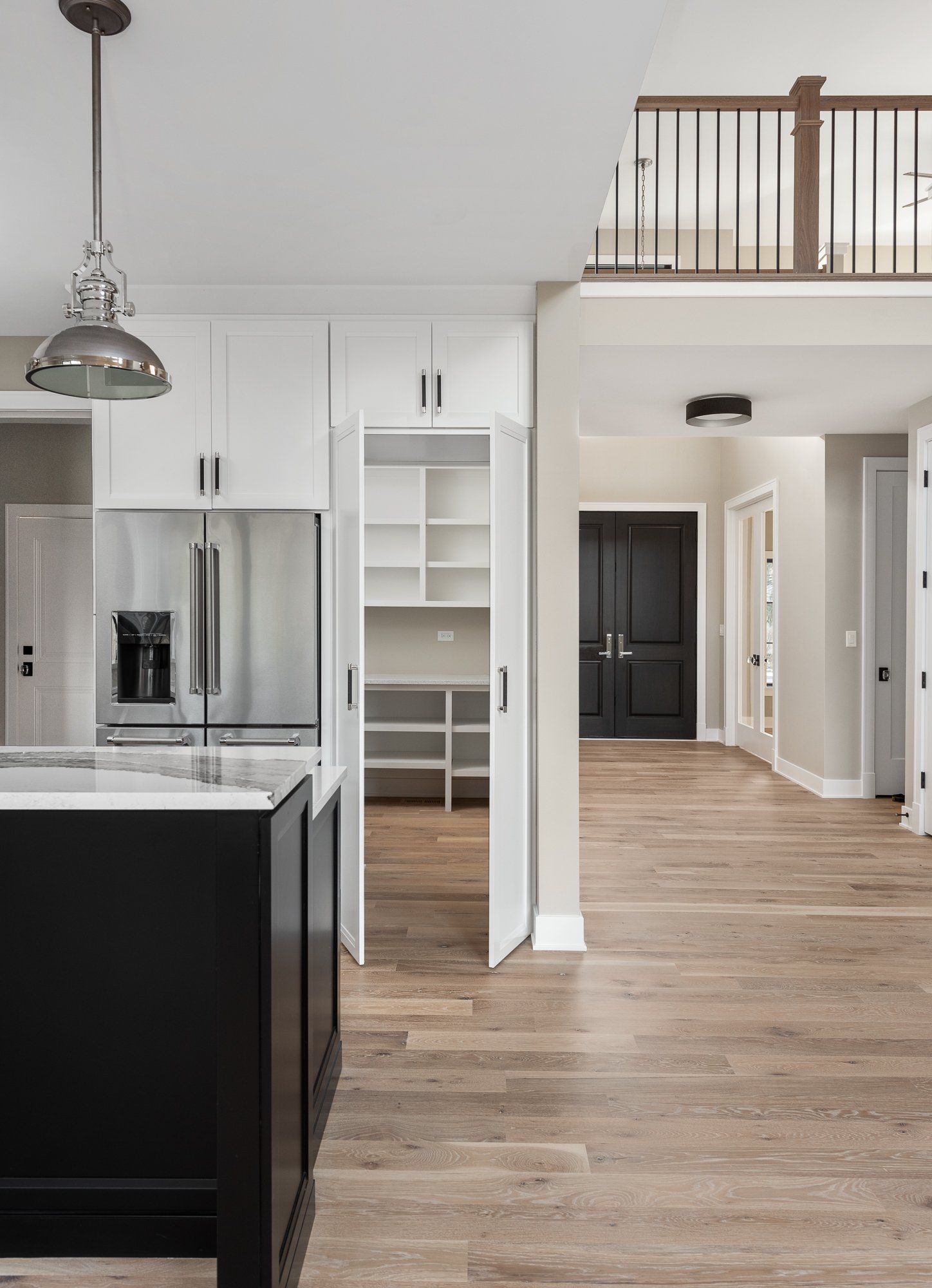 A kitchen with a black island , white cabinets , and hardwood floors.