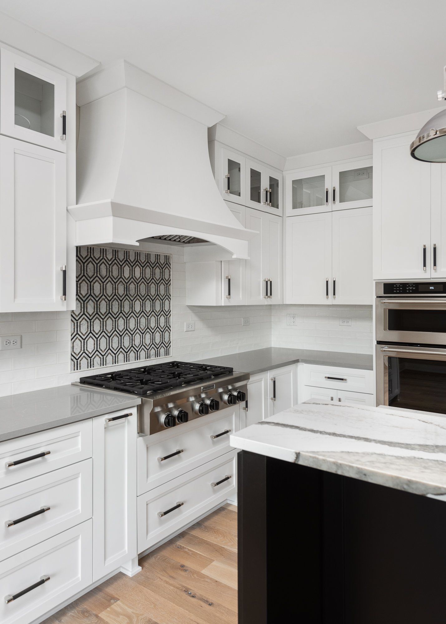 A kitchen with white cabinets , a stove , a microwave , and a black island.