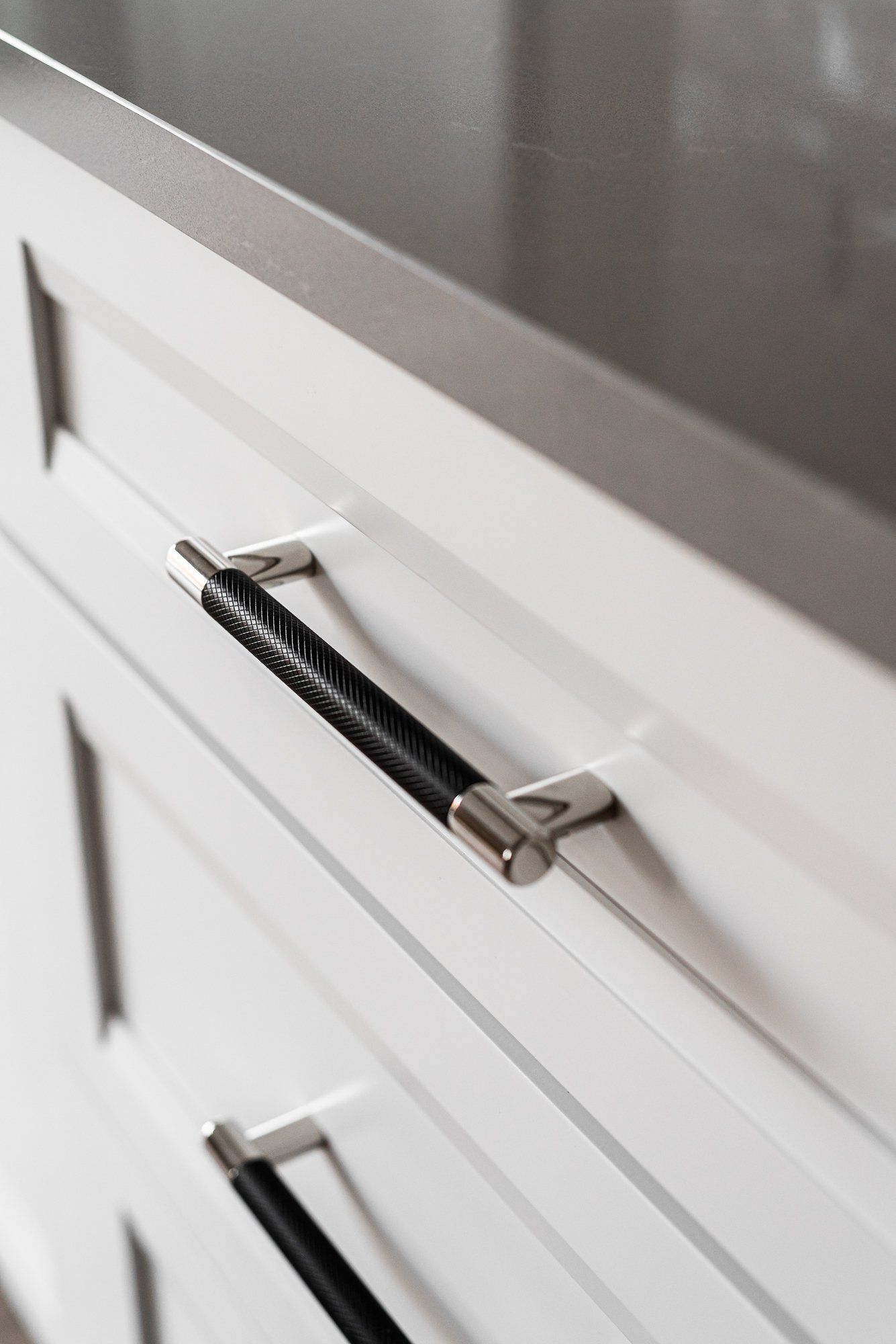 A close up of a white cabinet with black handles and a stainless steel counter top.