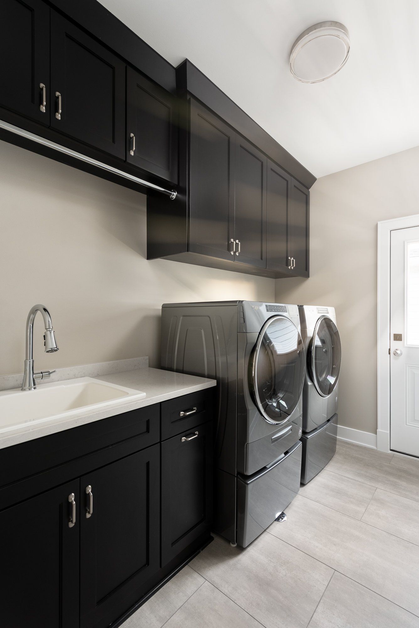 A laundry room with black cabinets , a washer and dryer , and a sink.