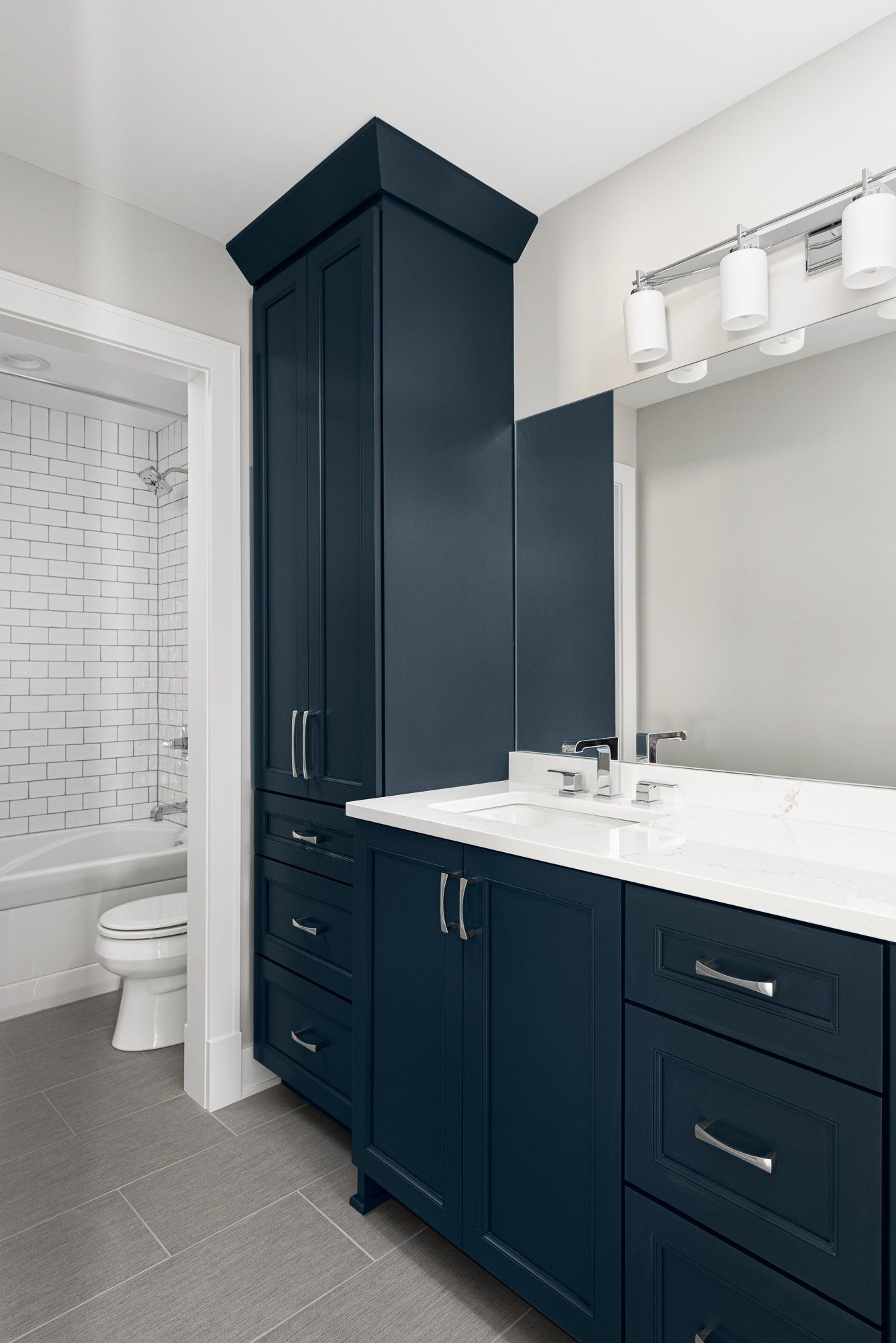 A bathroom with blue cabinets , a sink , a toilet , and a mirror.