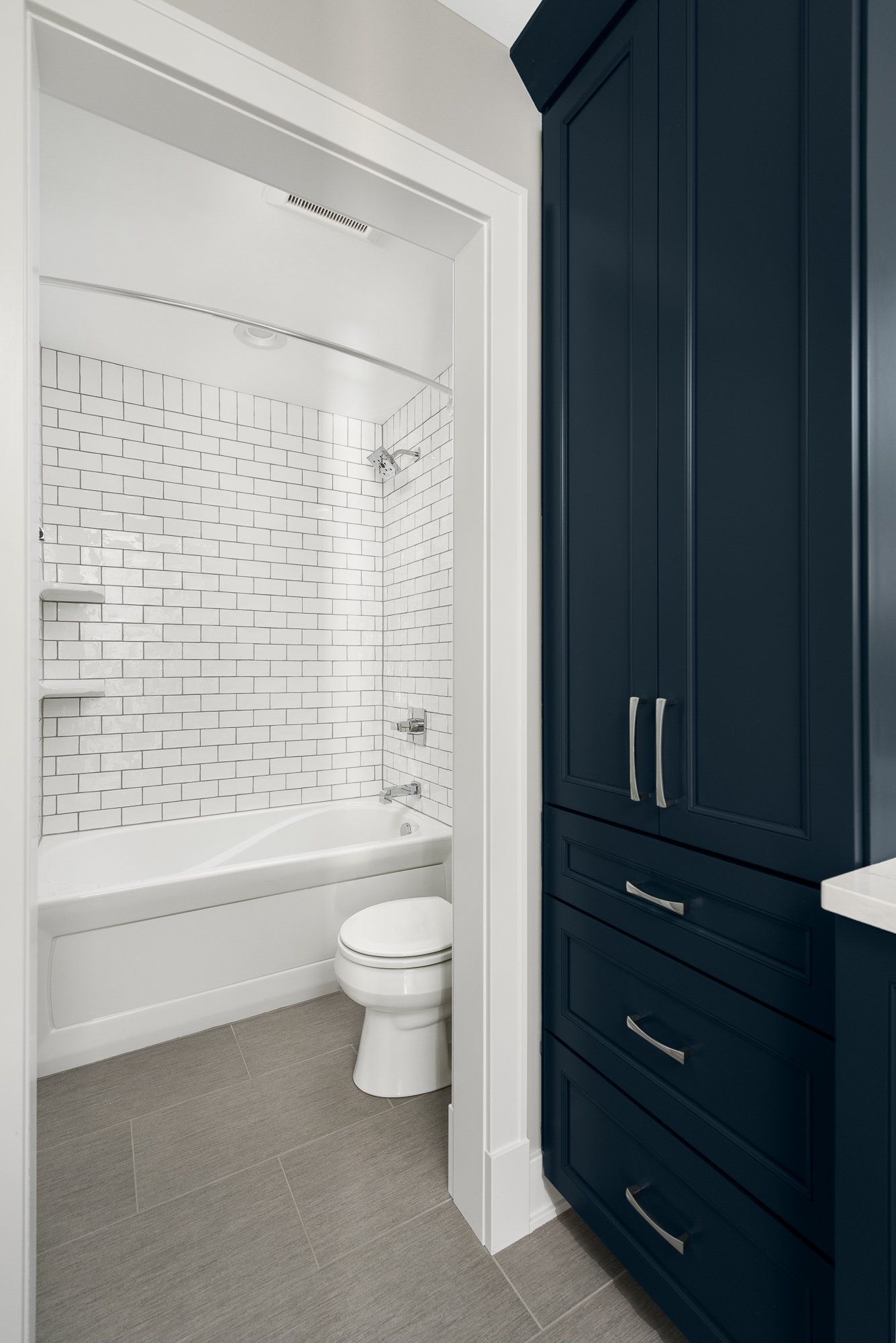 A bathroom with a toilet , bathtub and blue cabinets.
