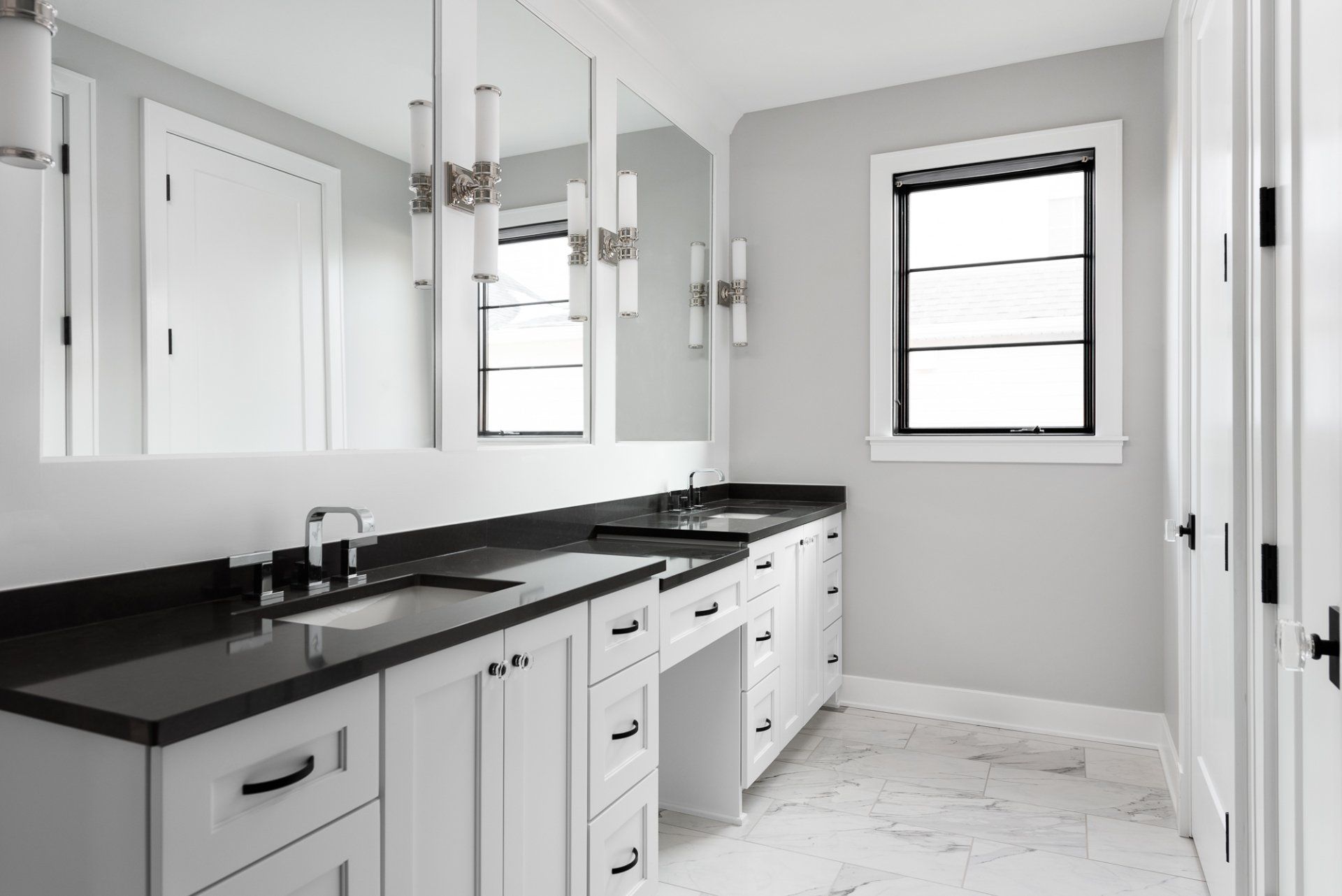 A bathroom with two sinks , two mirrors , and a window.