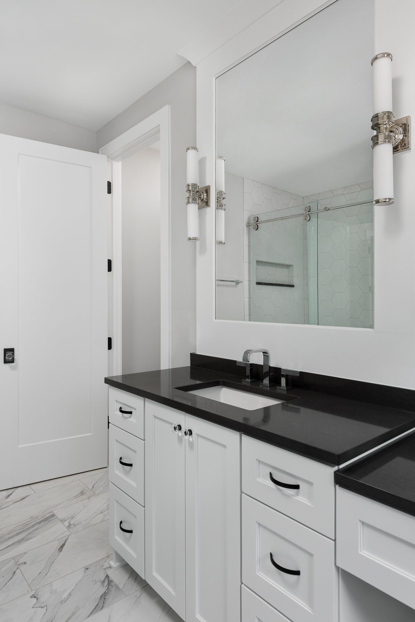 A bathroom with white cabinets , black counter tops , a sink and a mirror.