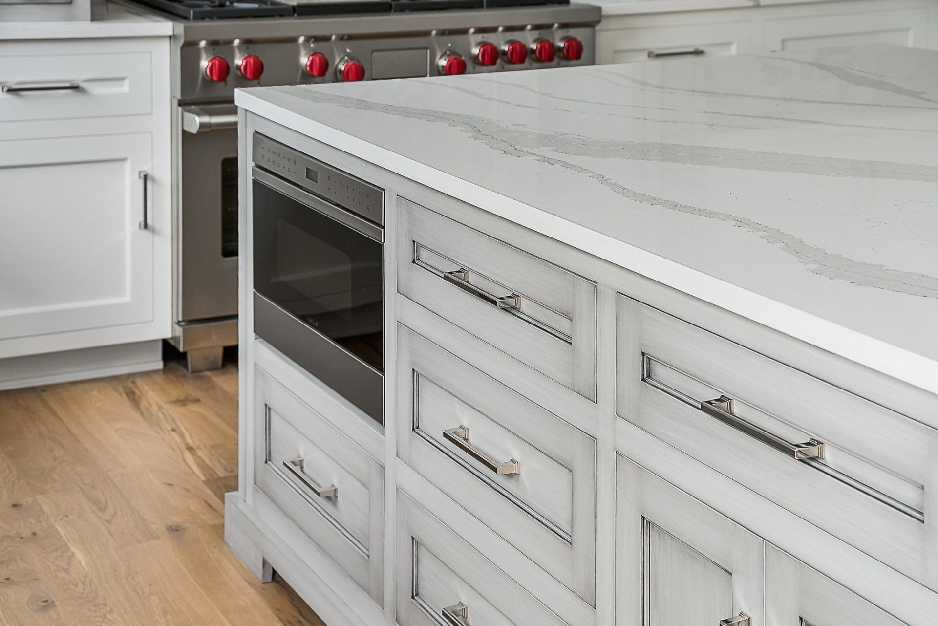 A kitchen with white cabinets , a stove , and a large island.