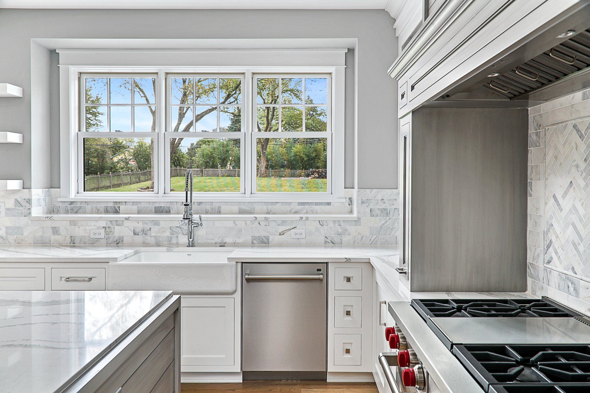 A kitchen with white cabinets , a stove , a sink , and a window.