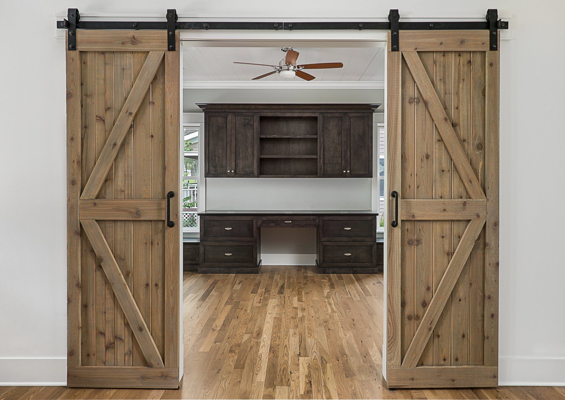 A room with sliding barn doors leading to a desk and cabinets.