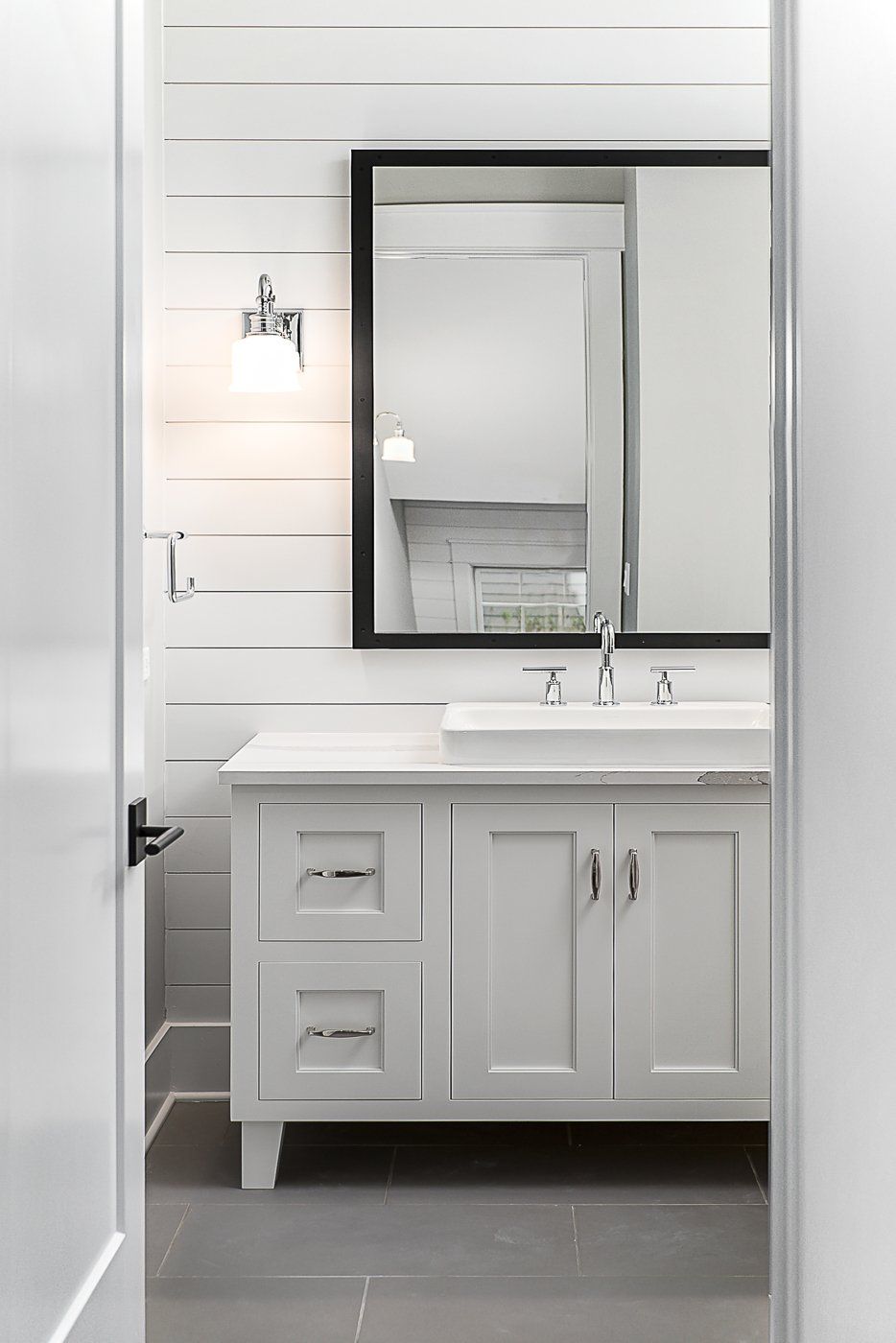 A bathroom with white cabinets , a sink and a mirror.