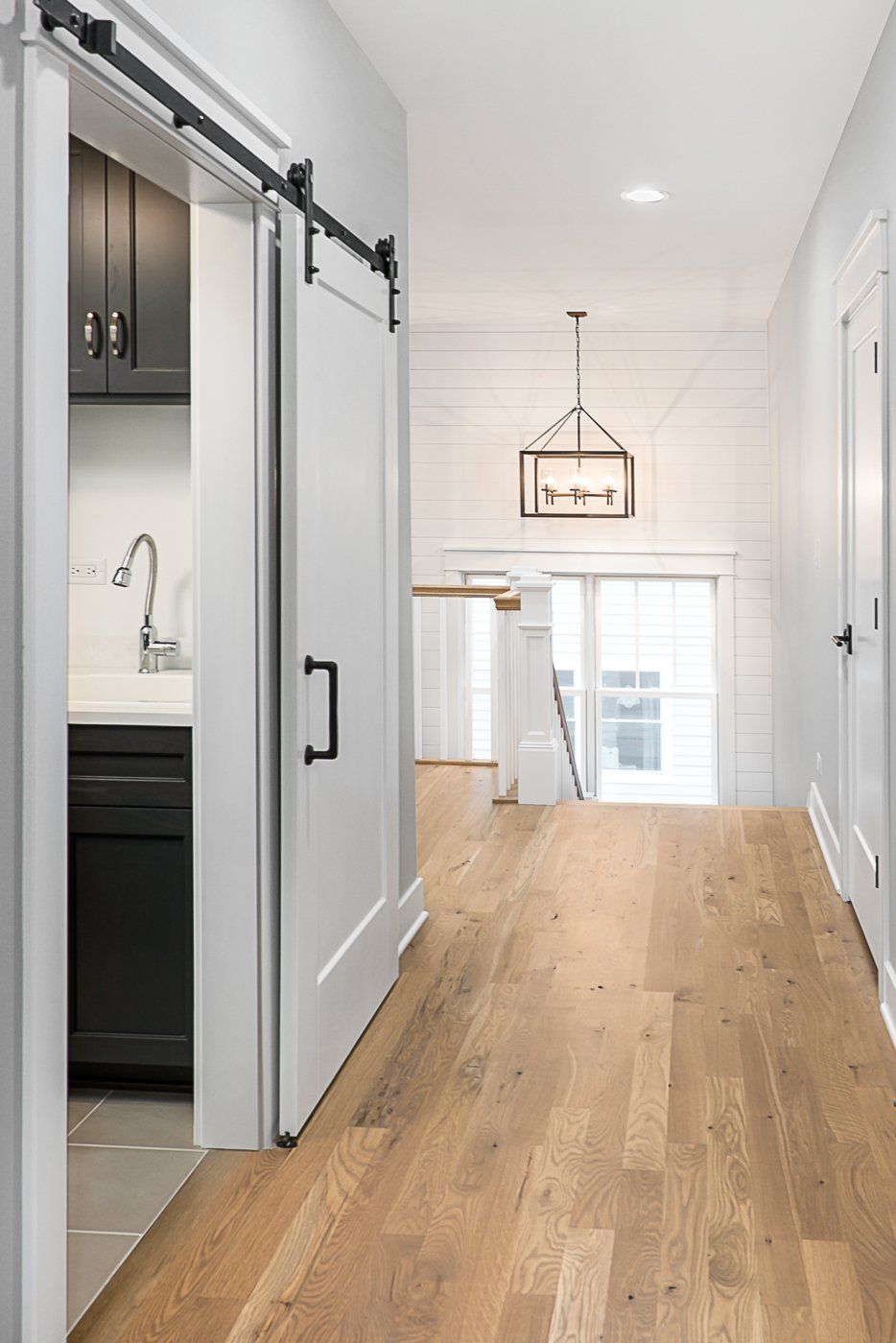 A hallway with hardwood floors and a sliding barn door leading to a kitchen.