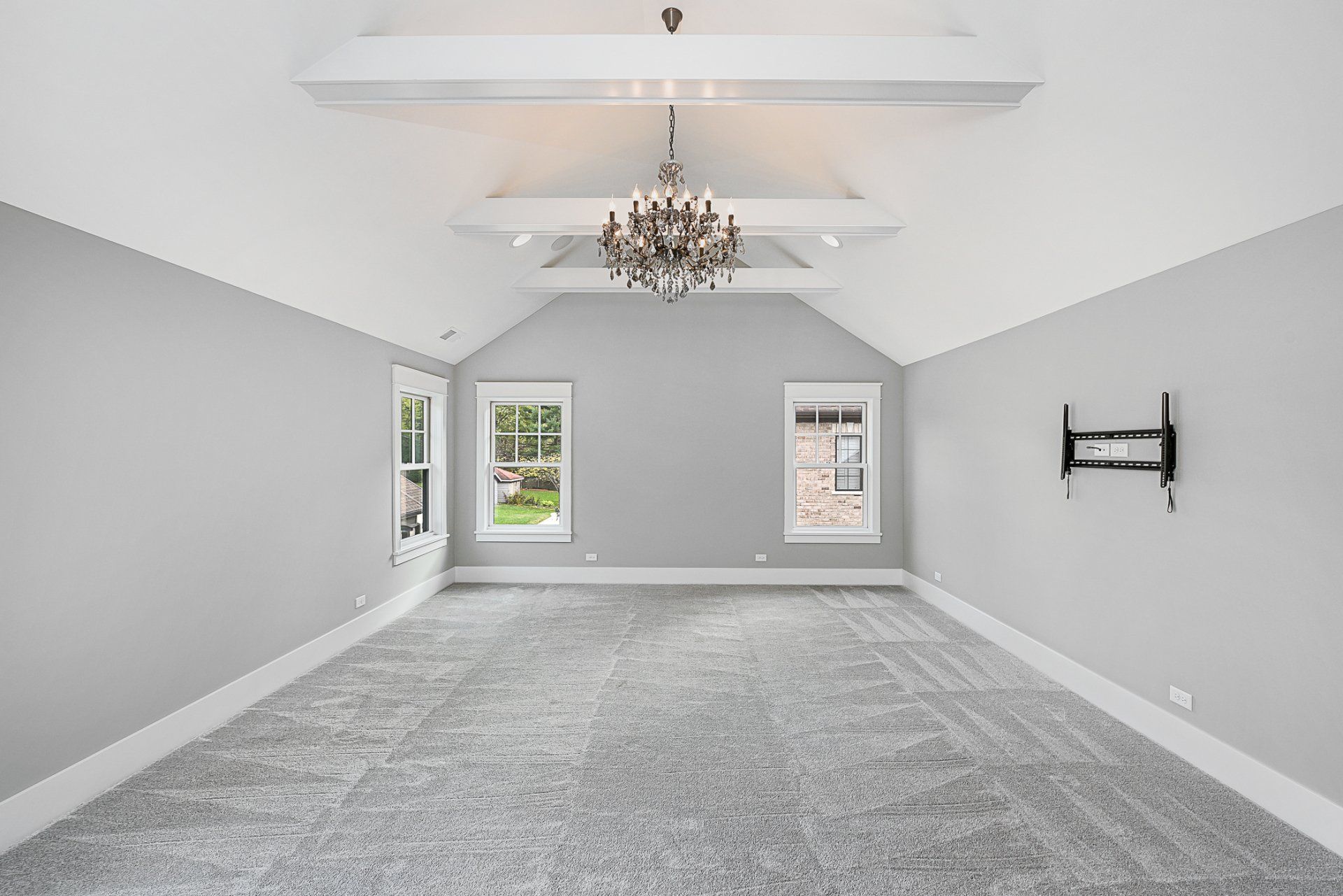 An empty room with a chandelier hanging from the ceiling and a flat screen tv mounted on the wall.