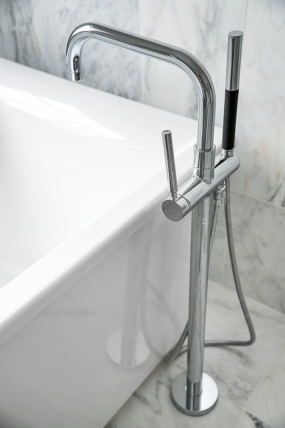 A bathtub with a chrome faucet and hose attached to it.