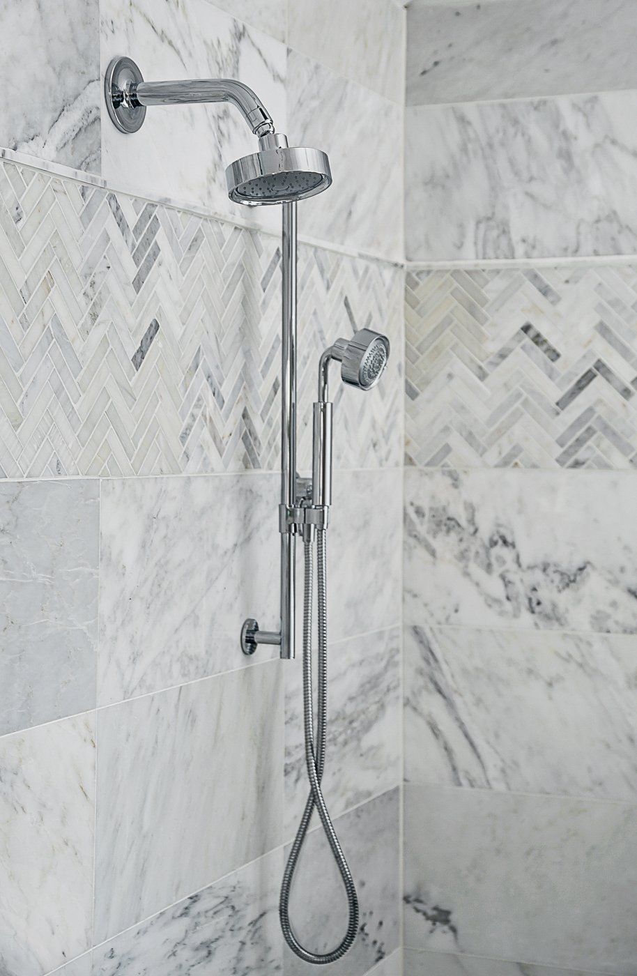 A close up of a shower head in a bathroom with marble tiles.