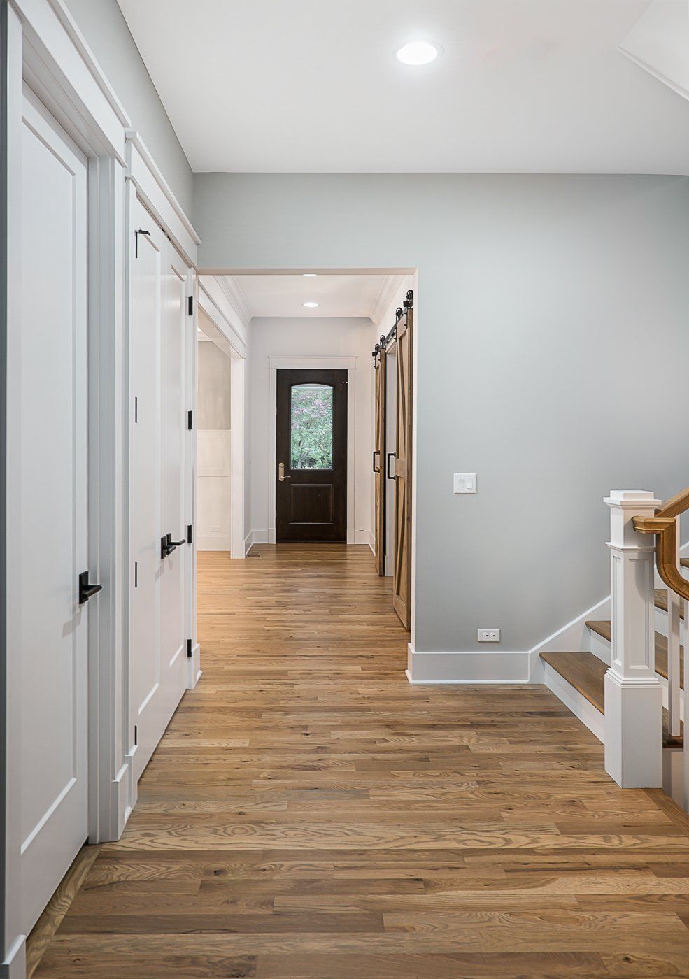 A hallway with hardwood floors and a staircase in a house.
