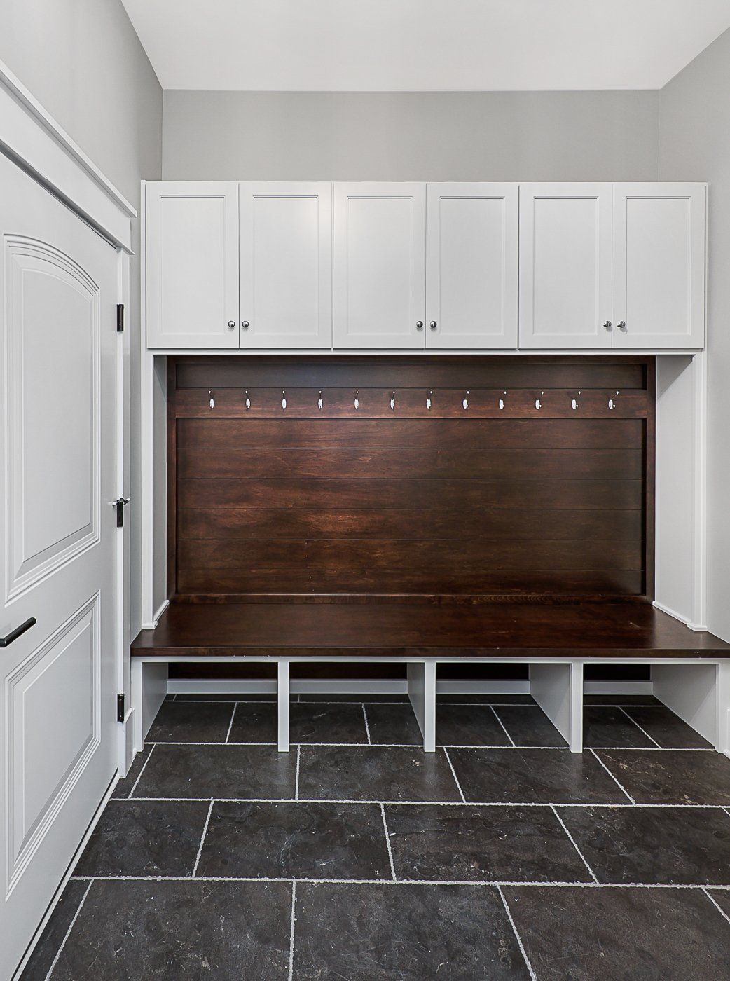 A mud room with a wooden bench and white cabinets