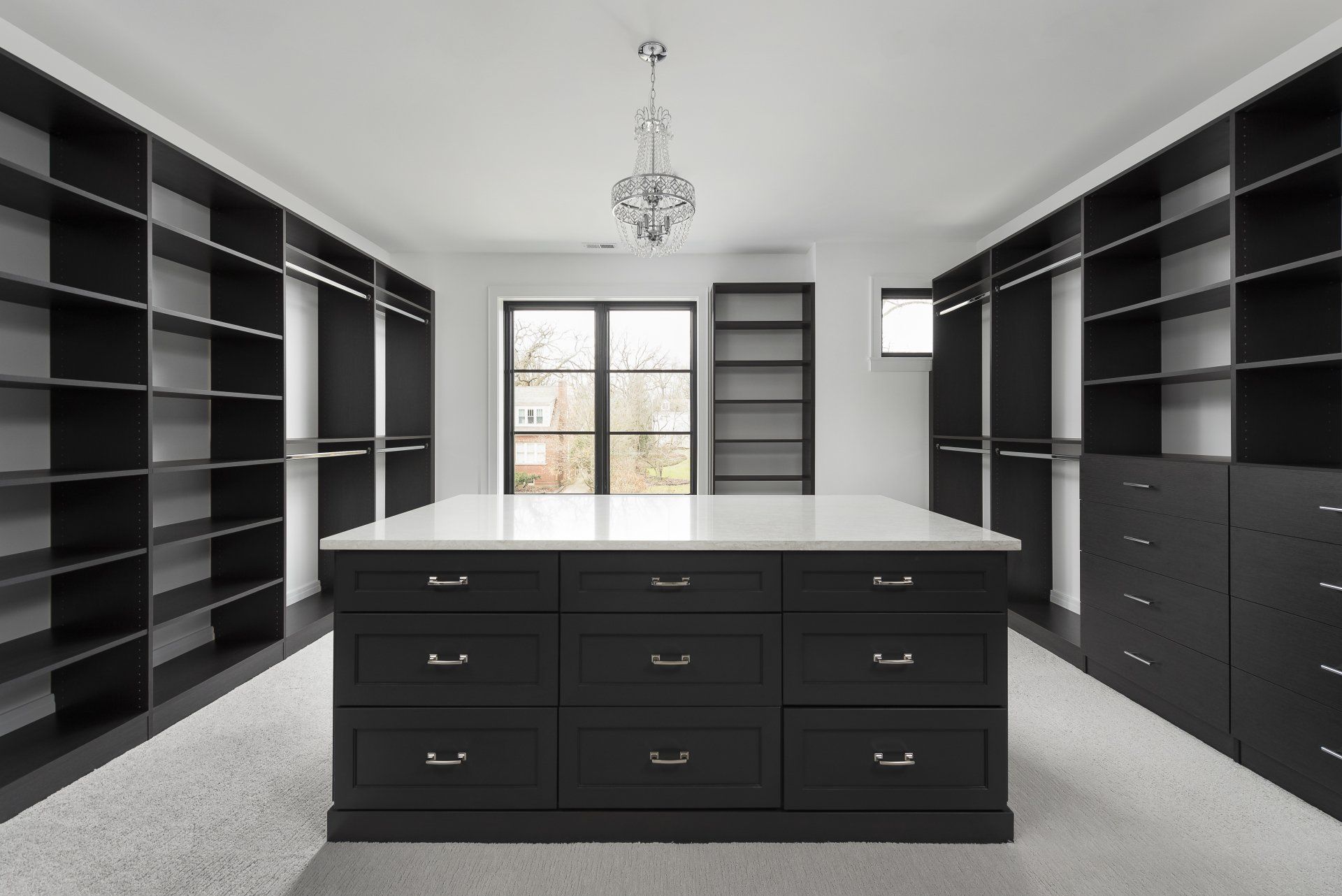 A large walk in closet with black shelves and drawers and a large island in the middle.