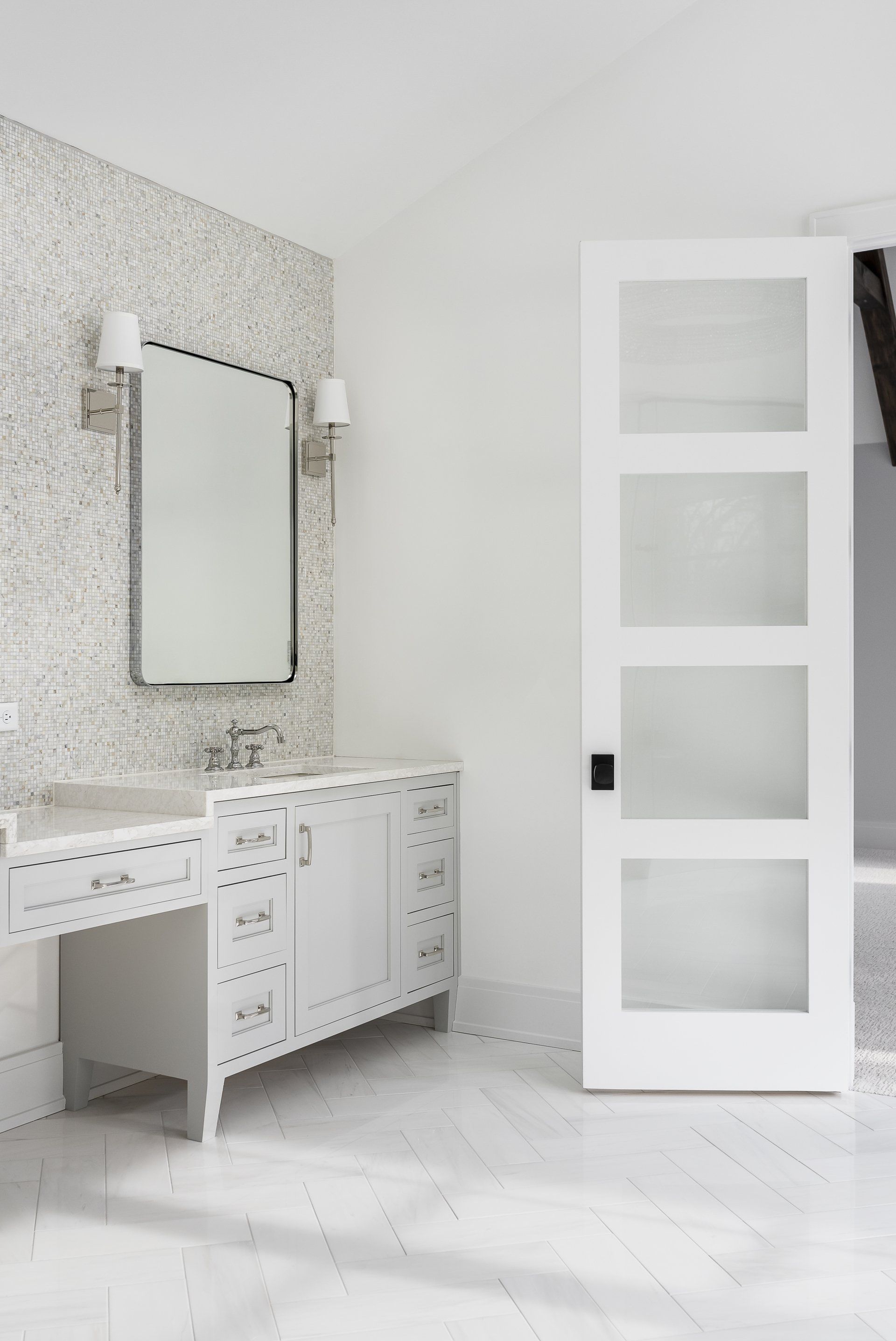 A bathroom with a vanity , mirror , and door.