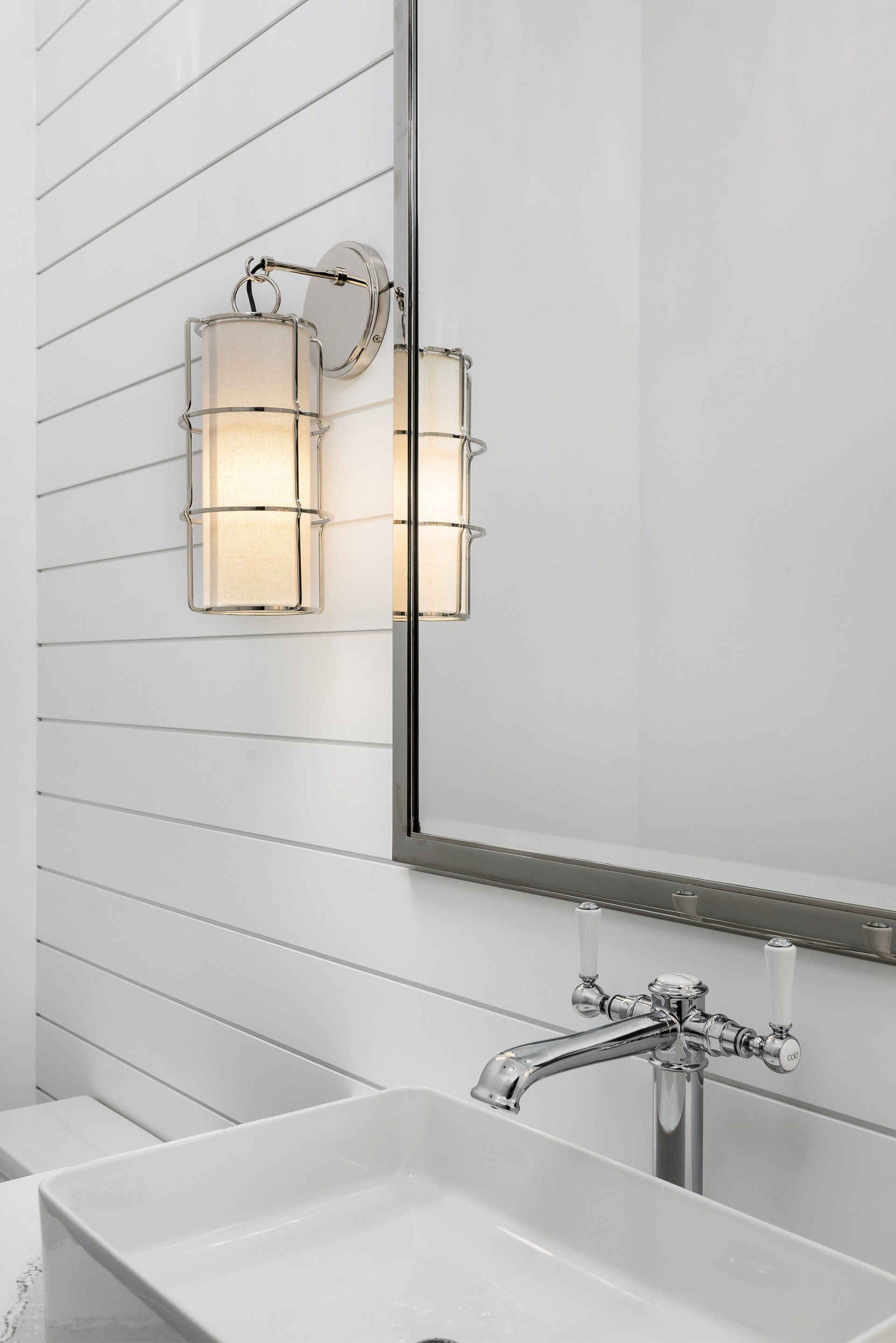 A bathroom with a sink , mirror and light on the wall