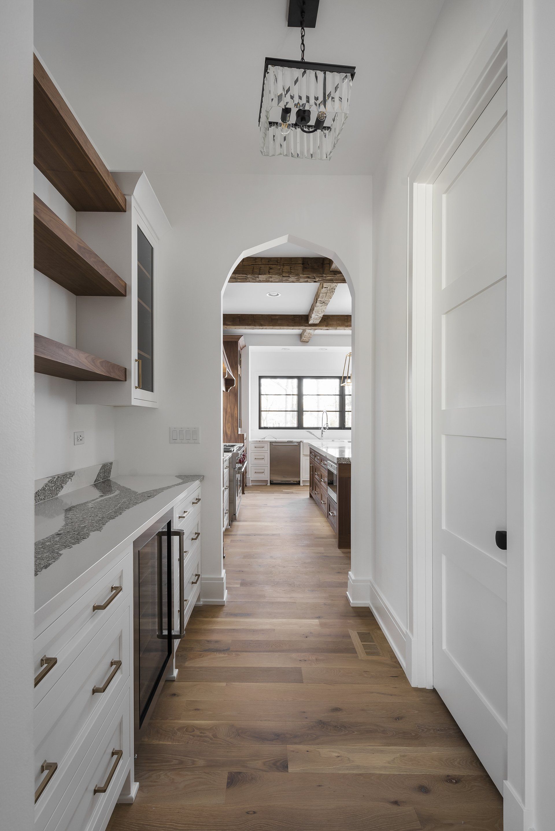 A hallway leading to a kitchen with white cabinets and wooden floors.