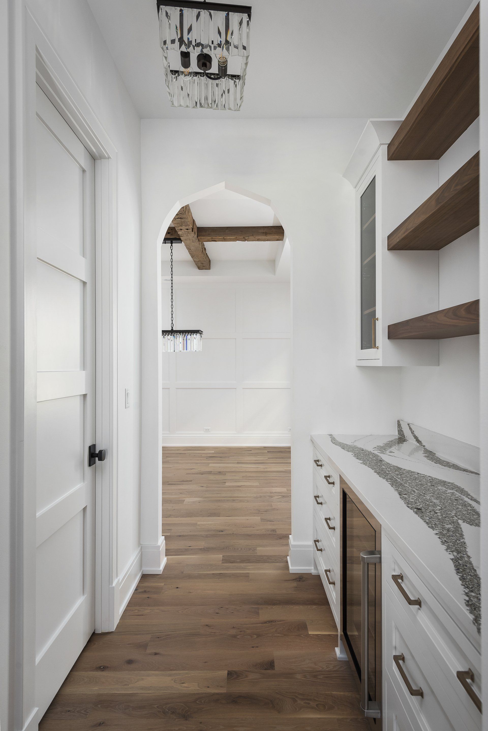 A hallway leading to a kitchen with white cabinets and wooden floors.