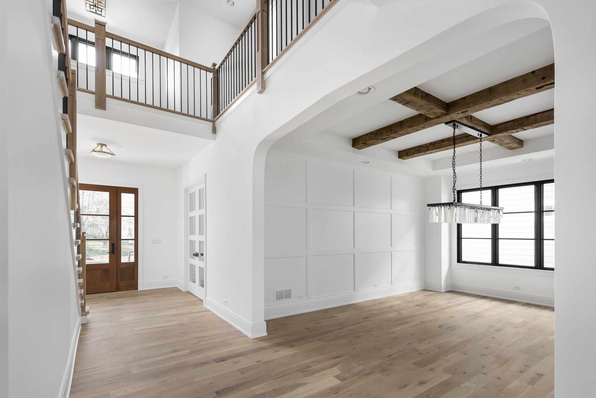 An empty living room with hardwood floors , white walls and wooden beams.
