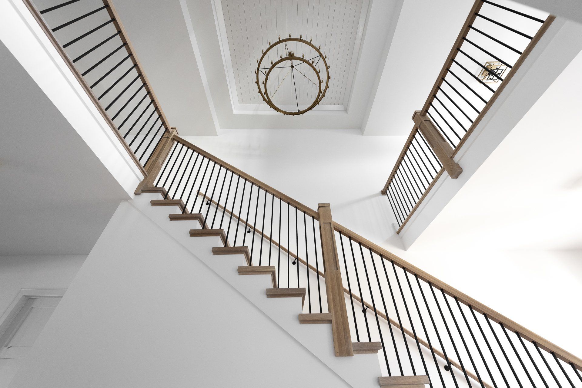 Looking up at a staircase with a chandelier hanging from the ceiling.