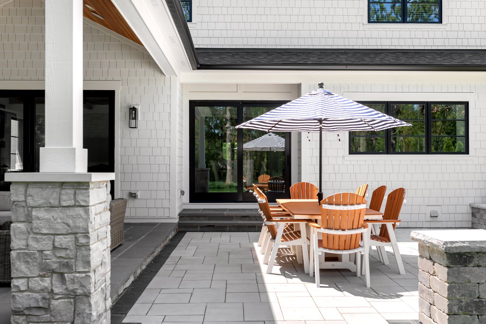 A patio with a table and chairs and umbrellas in front of a house.