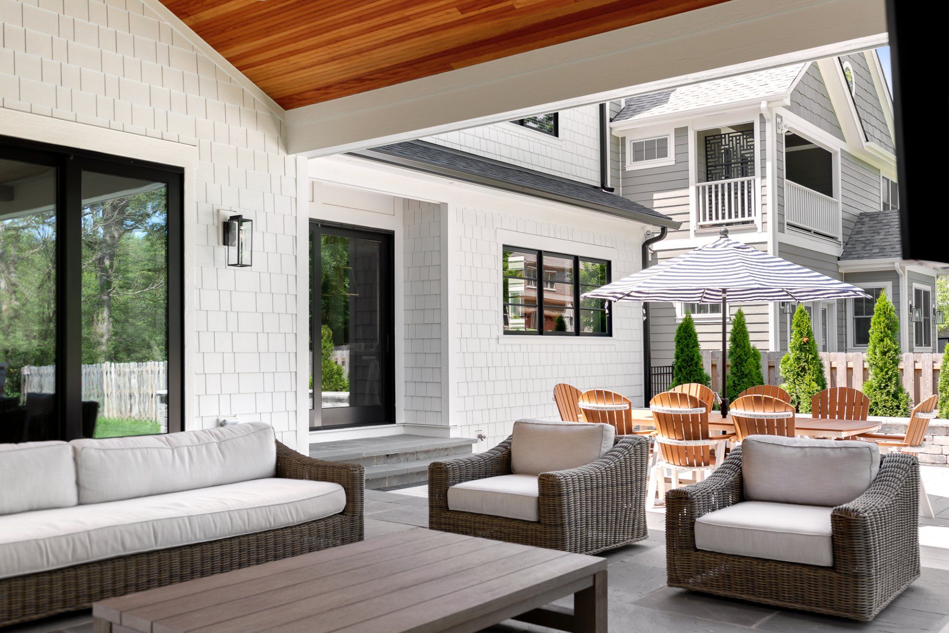 A patio with a couch , chairs , tables and umbrellas in front of a house.