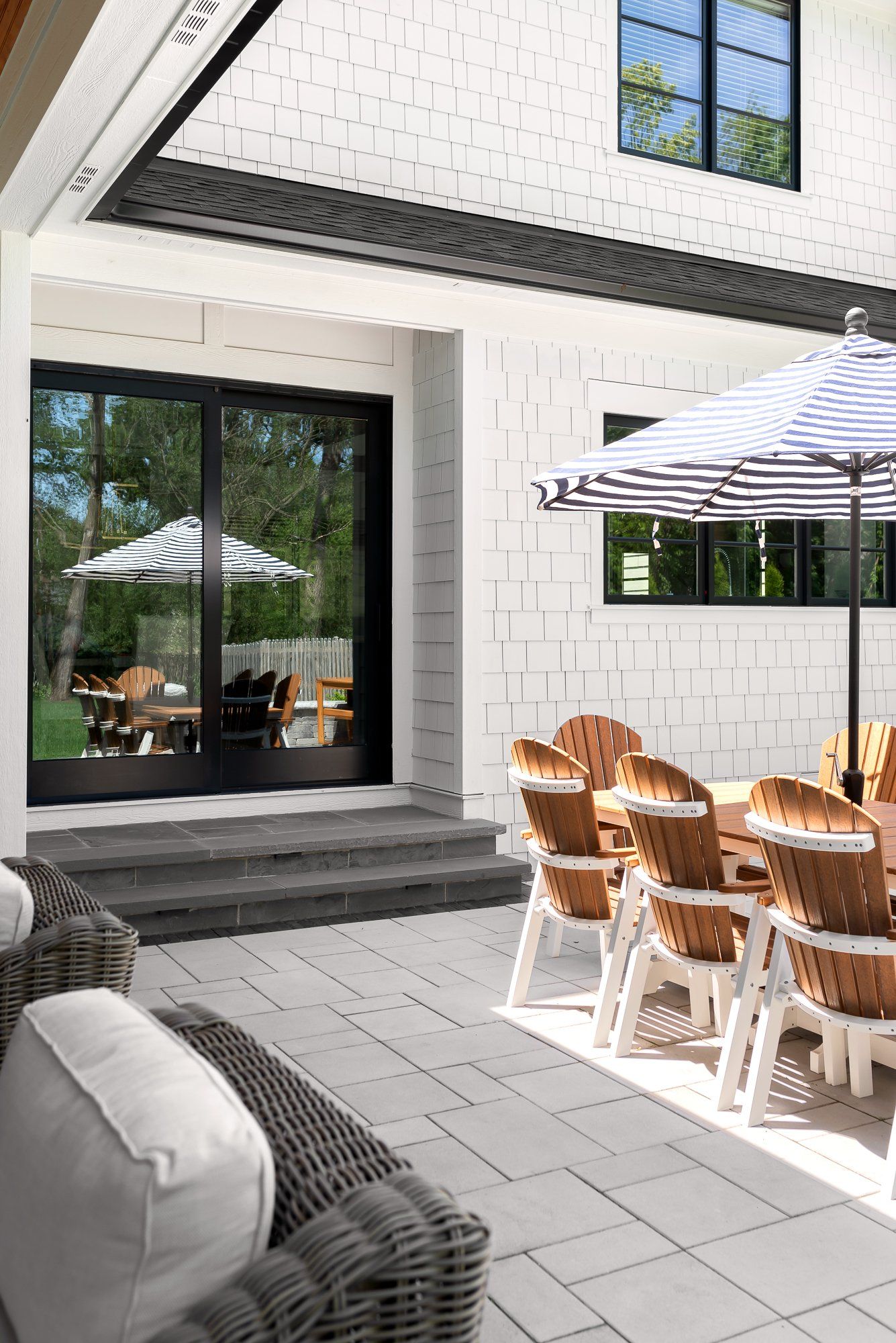 A patio with a table and chairs and umbrellas in front of a white brick house.