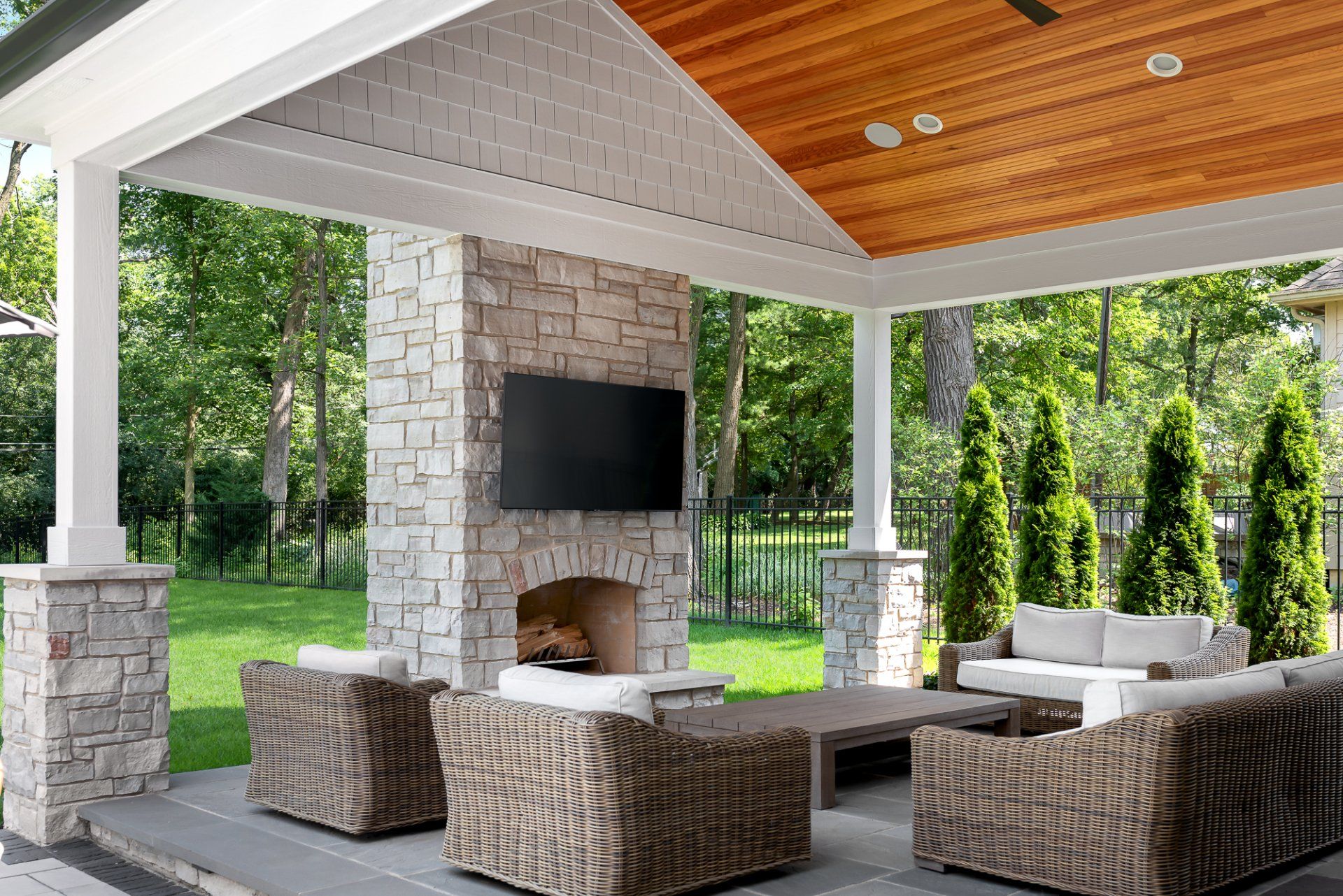 A patio with wicker furniture , a fireplace and a flat screen tv.