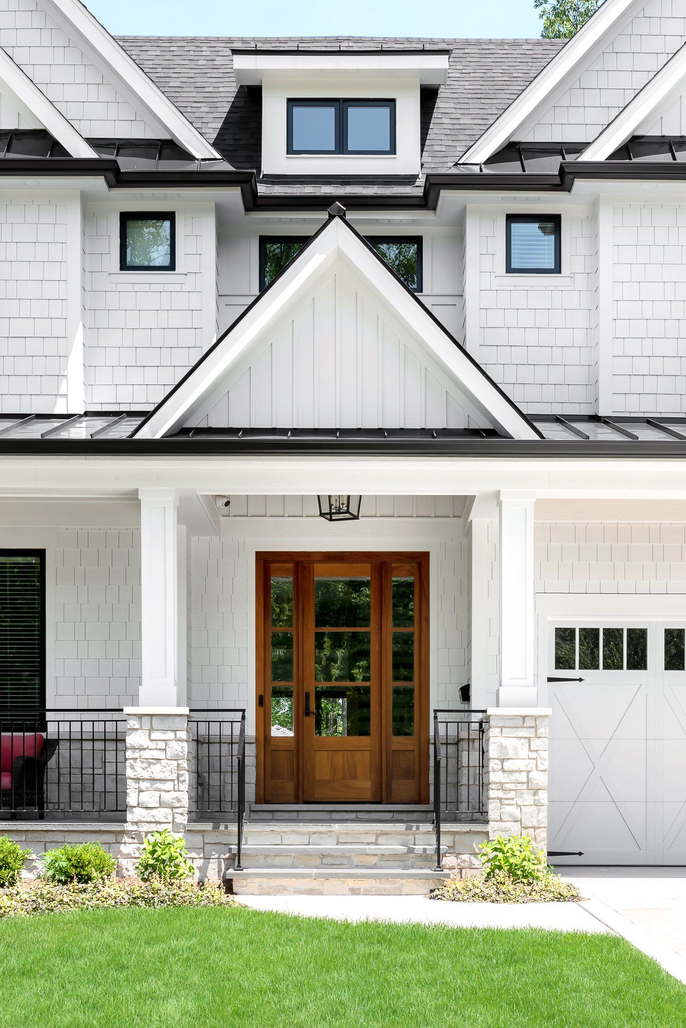 The front of a white house with a wooden door and a large porch.
