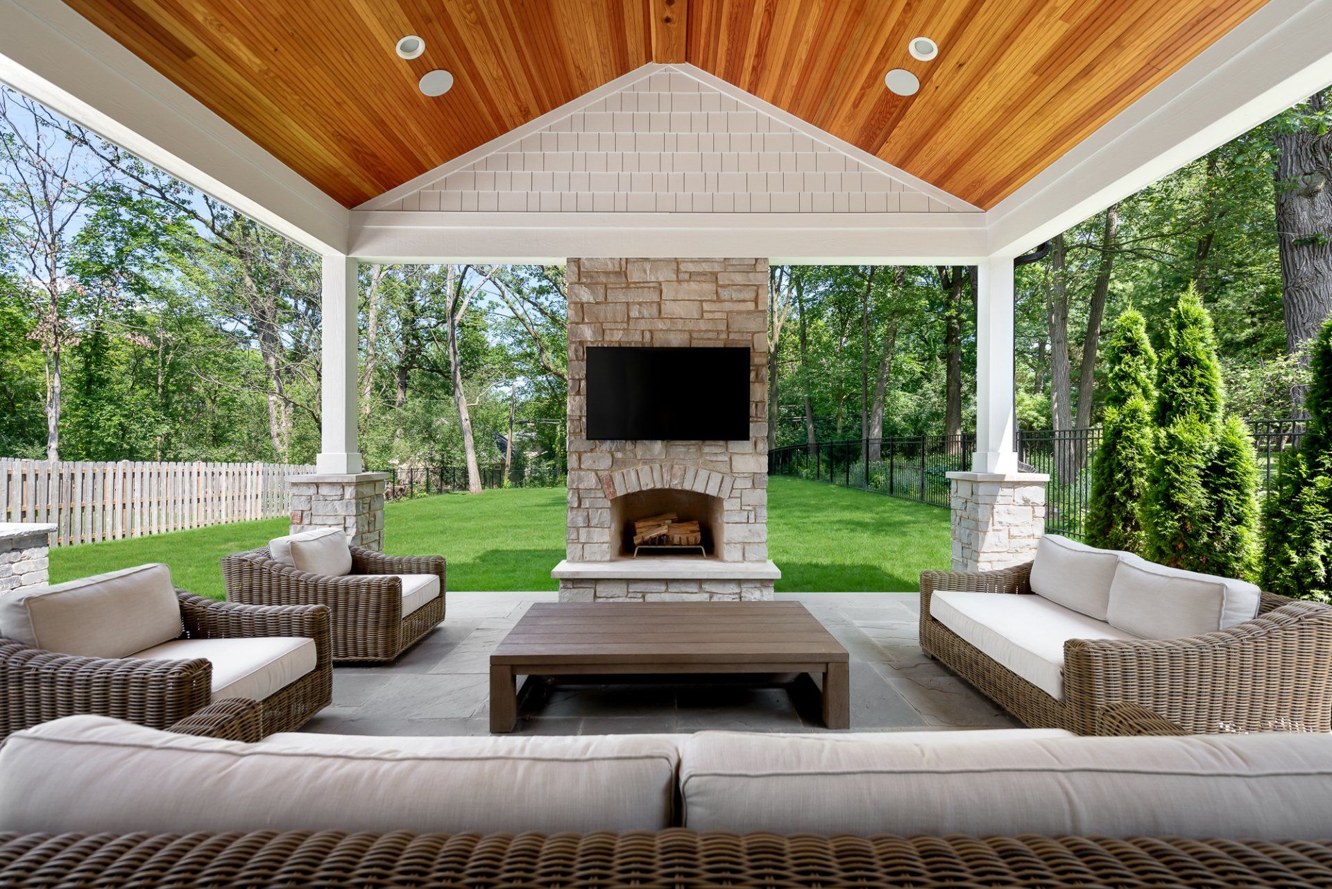 A patio with a fireplace , couch , chairs , table and television.