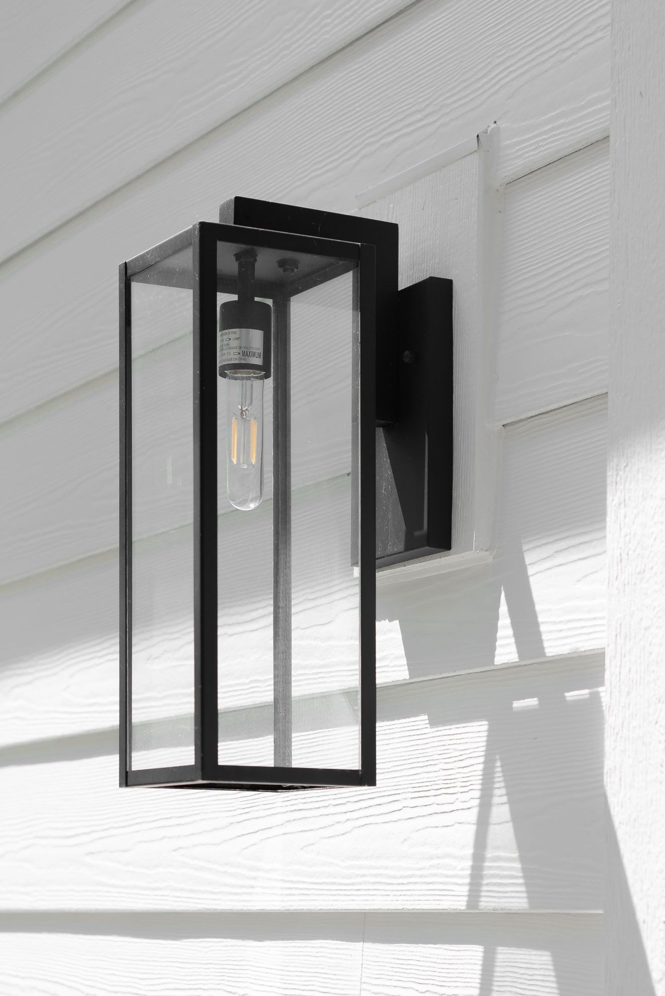 A black wall light with a clear glass shade is hanging on a white wall.