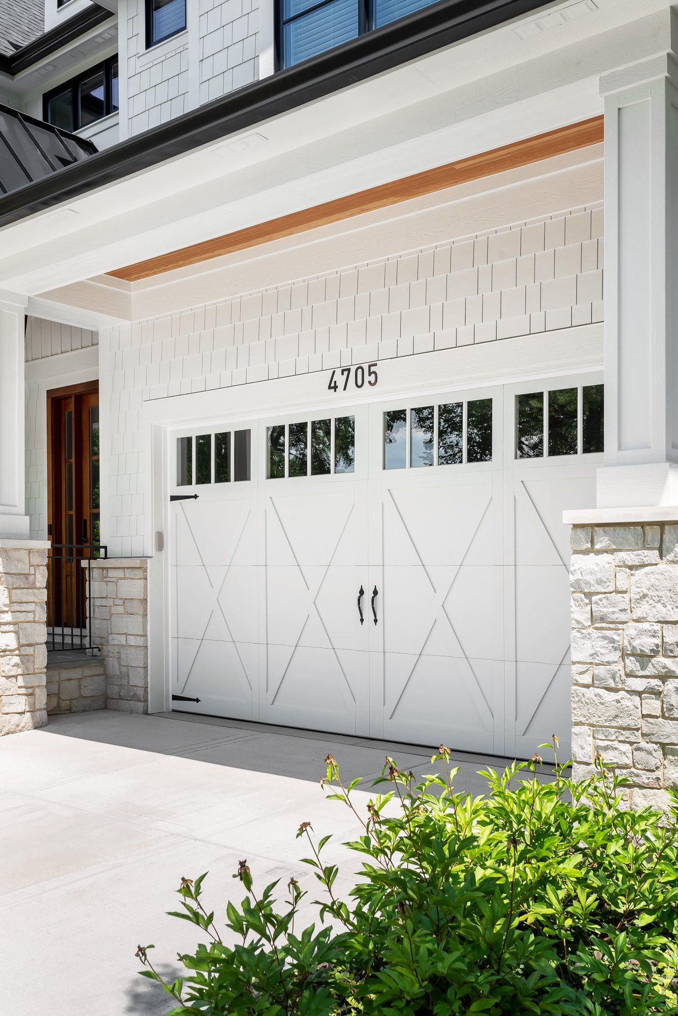 A white garage door is sitting under a porch of a house.