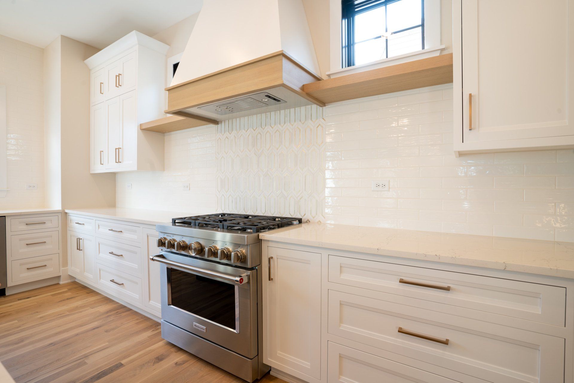 A kitchen with white cabinets , a stove , and a window.