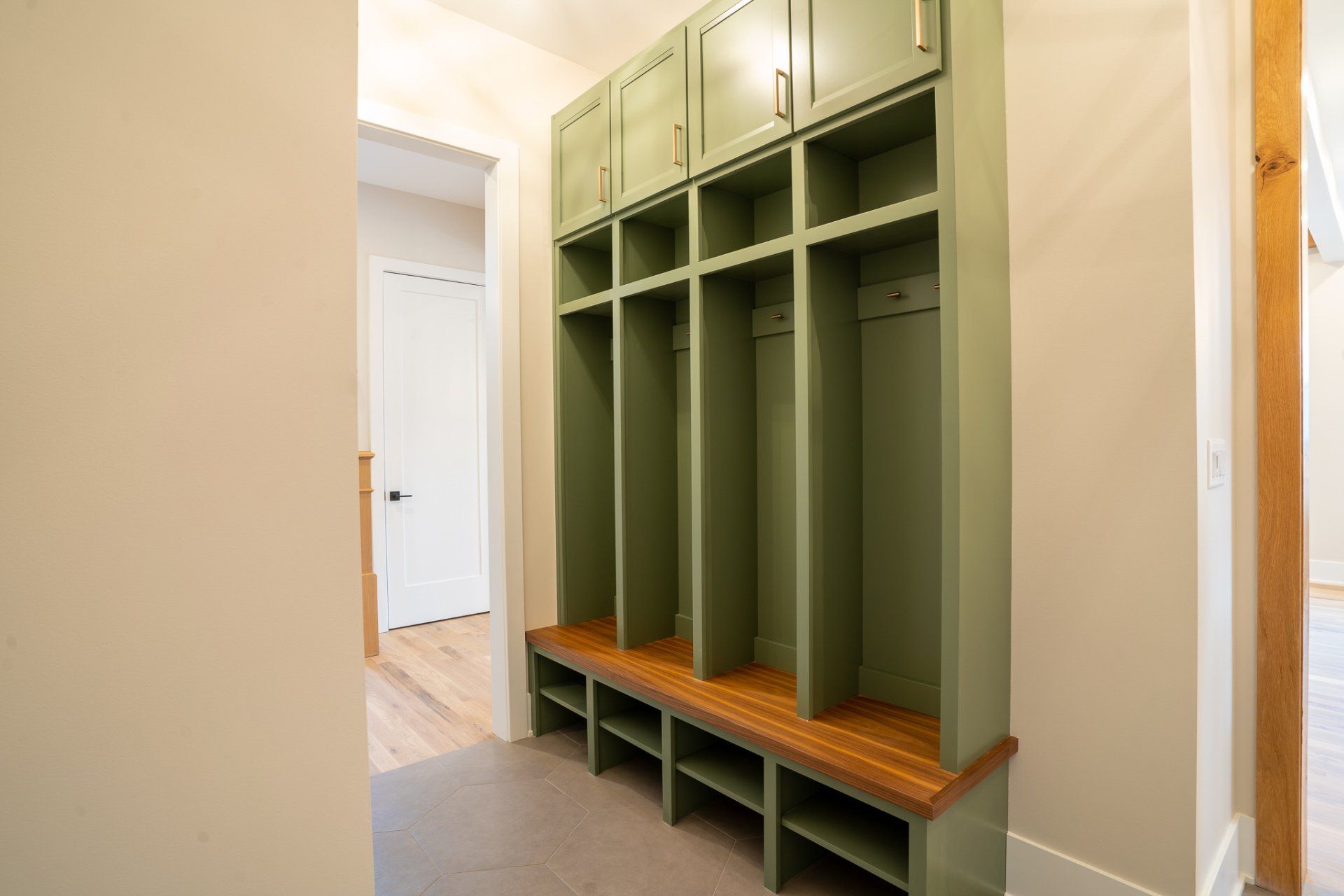 A green locker with a wooden bench in a hallway.