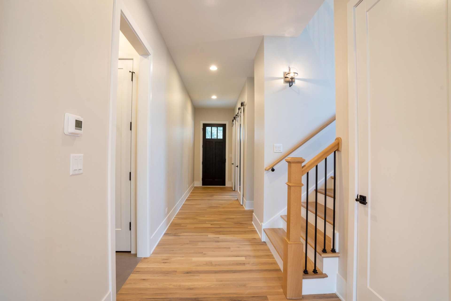 A long hallway with wooden floors and stairs in a house.