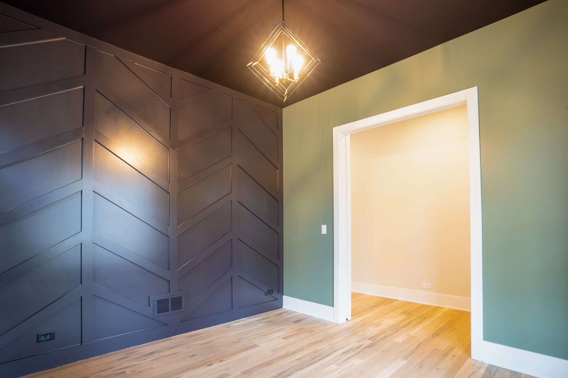 An empty room with wooden floors and a chandelier hanging from the ceiling.