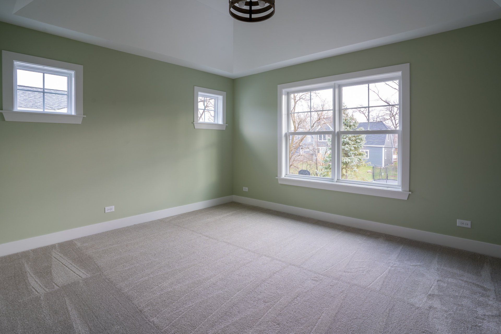 An empty bedroom with green walls and two windows.