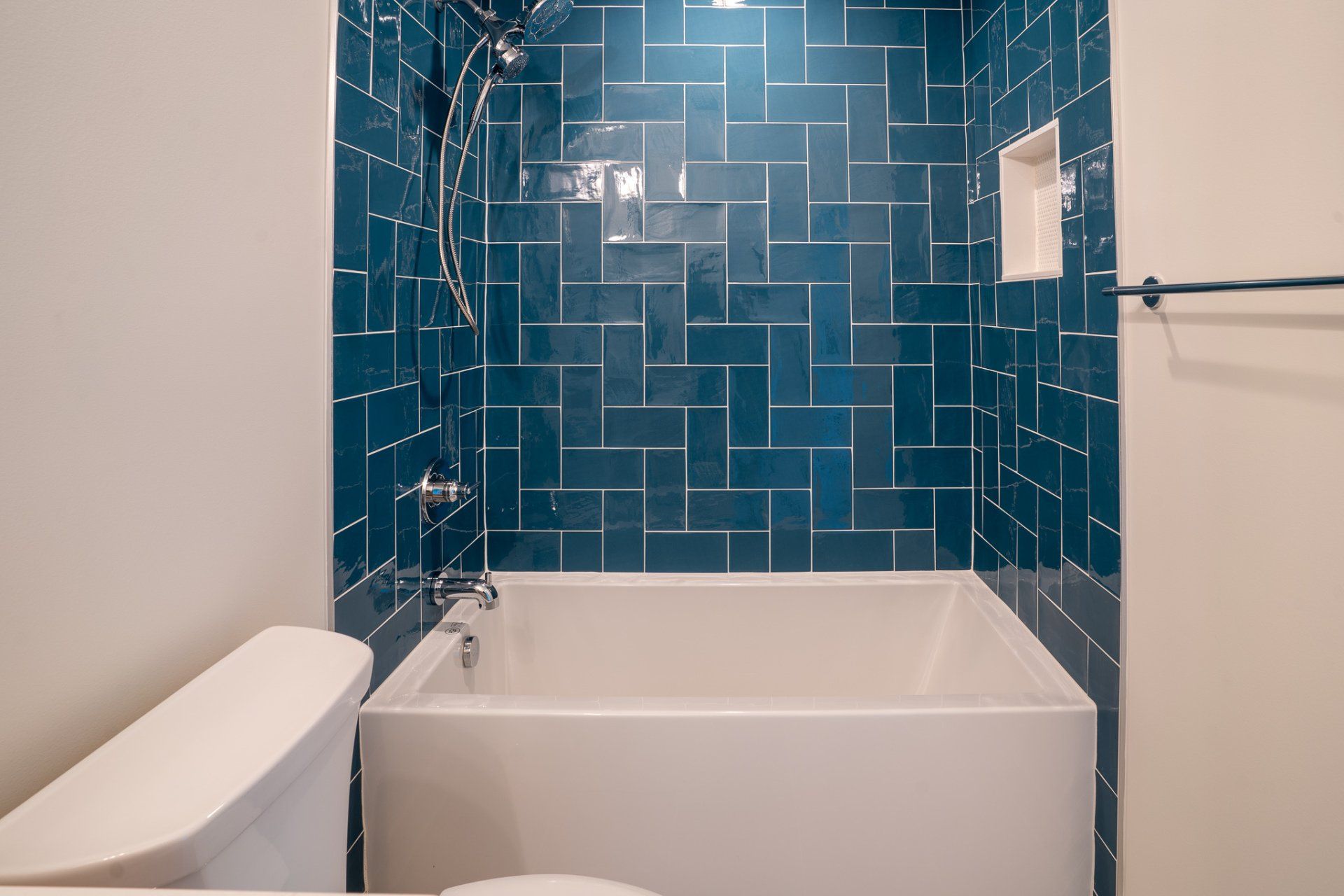 A bathroom with a bathtub , toilet , shower and blue tiles.