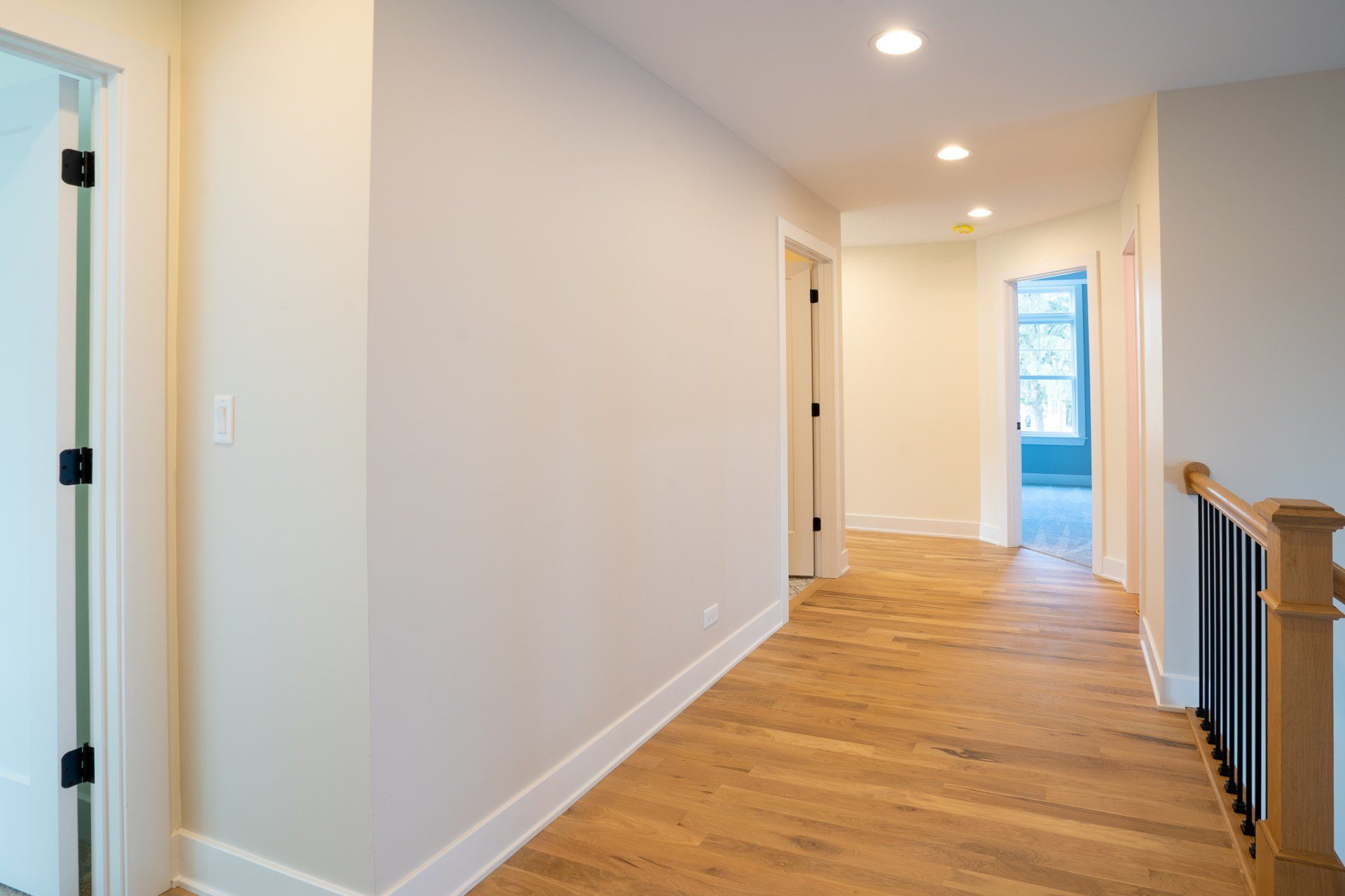 A long hallway with wooden floors and white walls in a house.