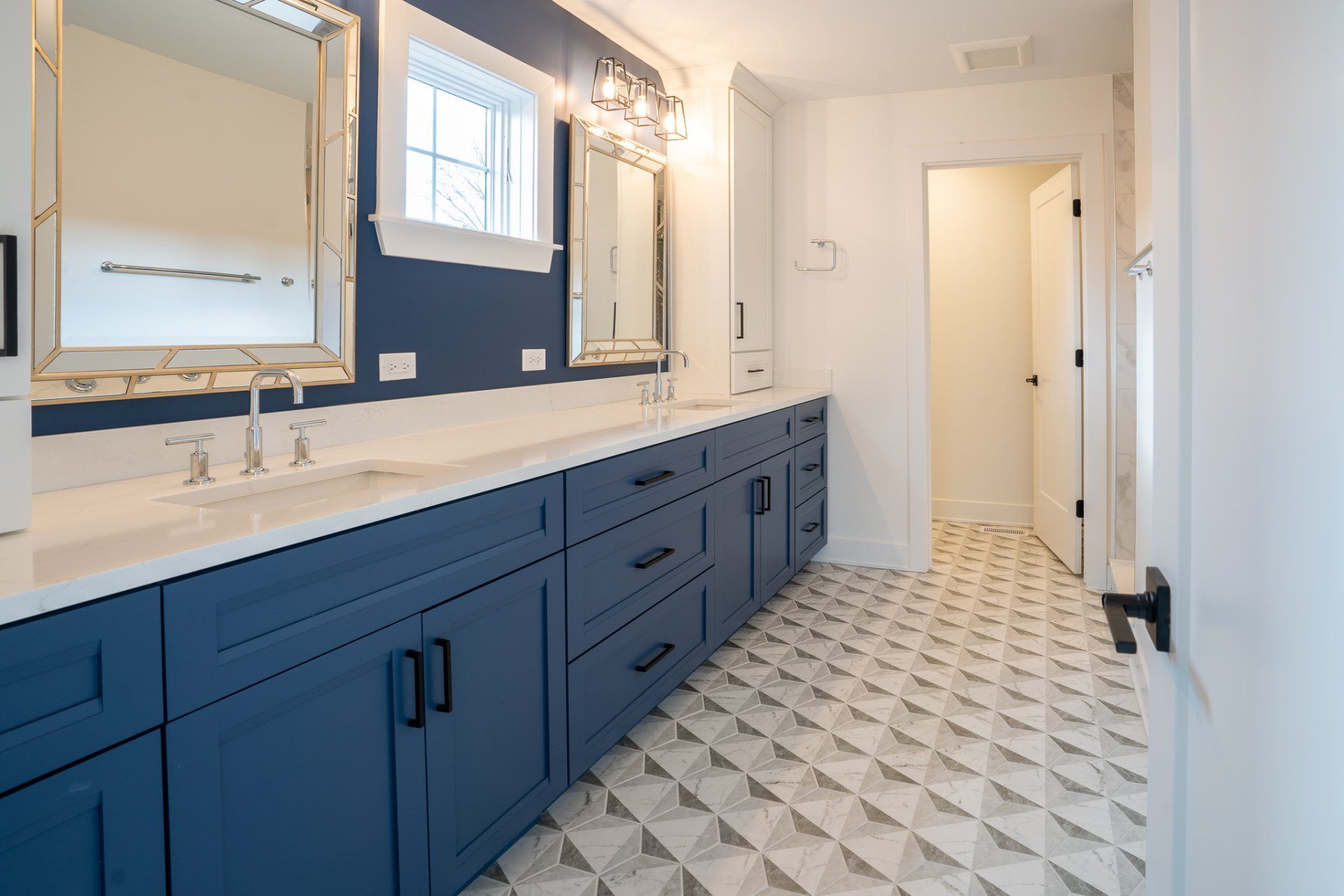A bathroom with blue cabinets , white counter tops , two sinks and two mirrors.