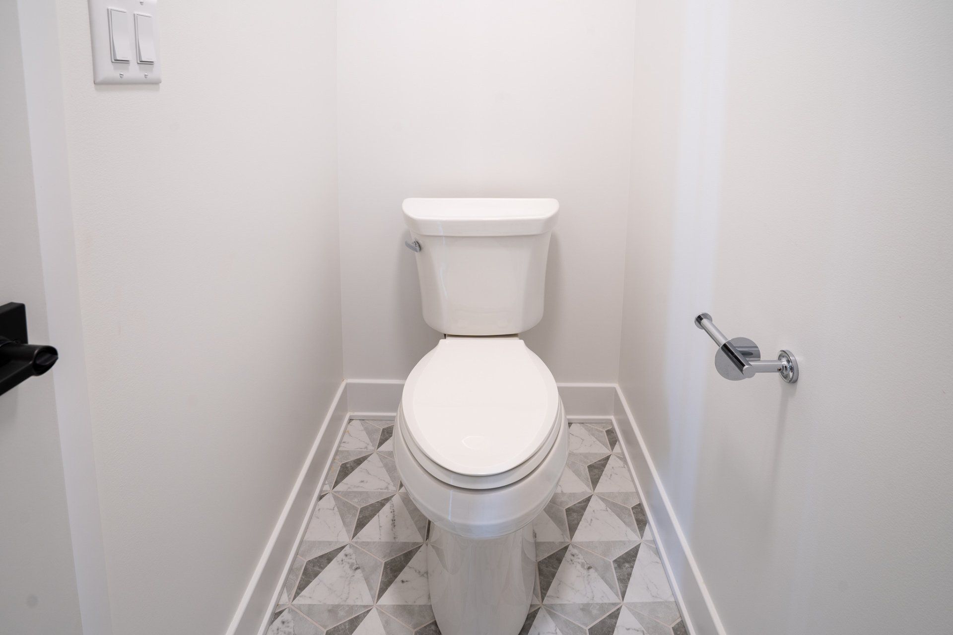 A toilet is sitting in a small bathroom with a patterned floor.