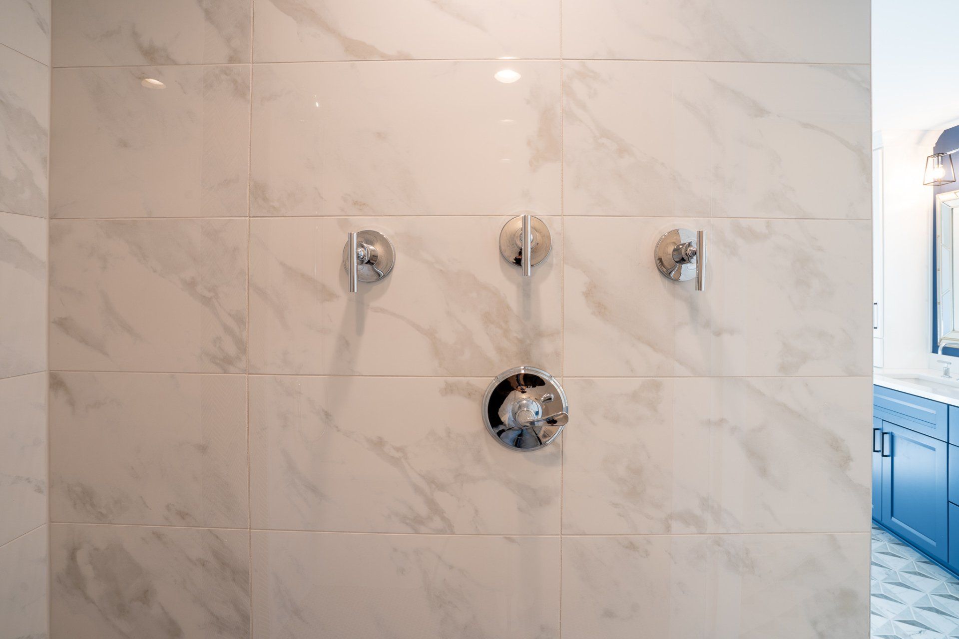 A bathroom with white tiles and chrome shower faucets.