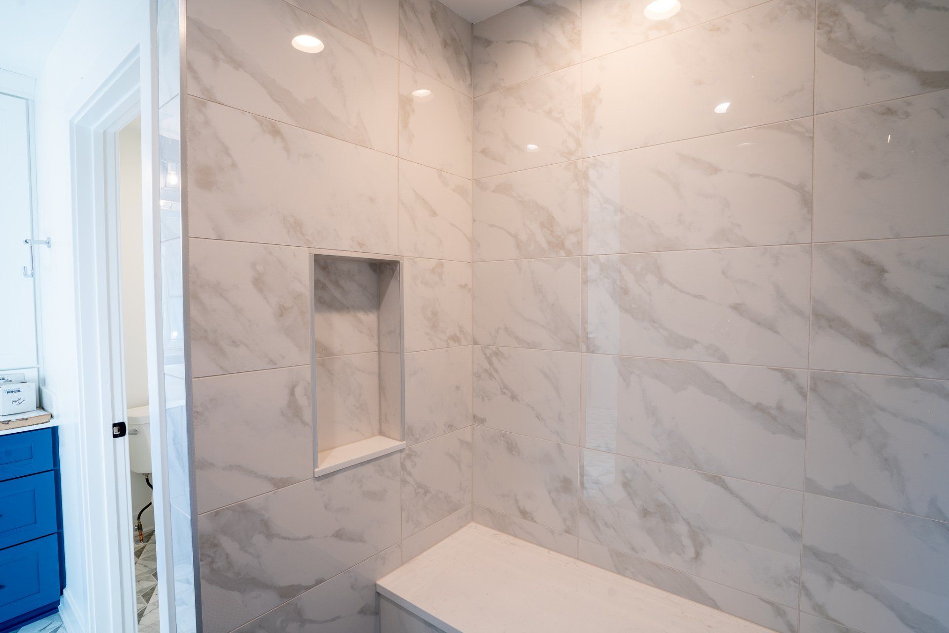 A bathroom with marble tiles and a bench in the shower.