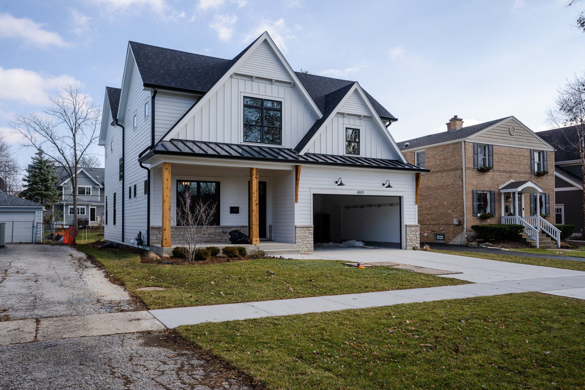 A white house with a black roof and a garage is sitting on top of a lush green lawn.