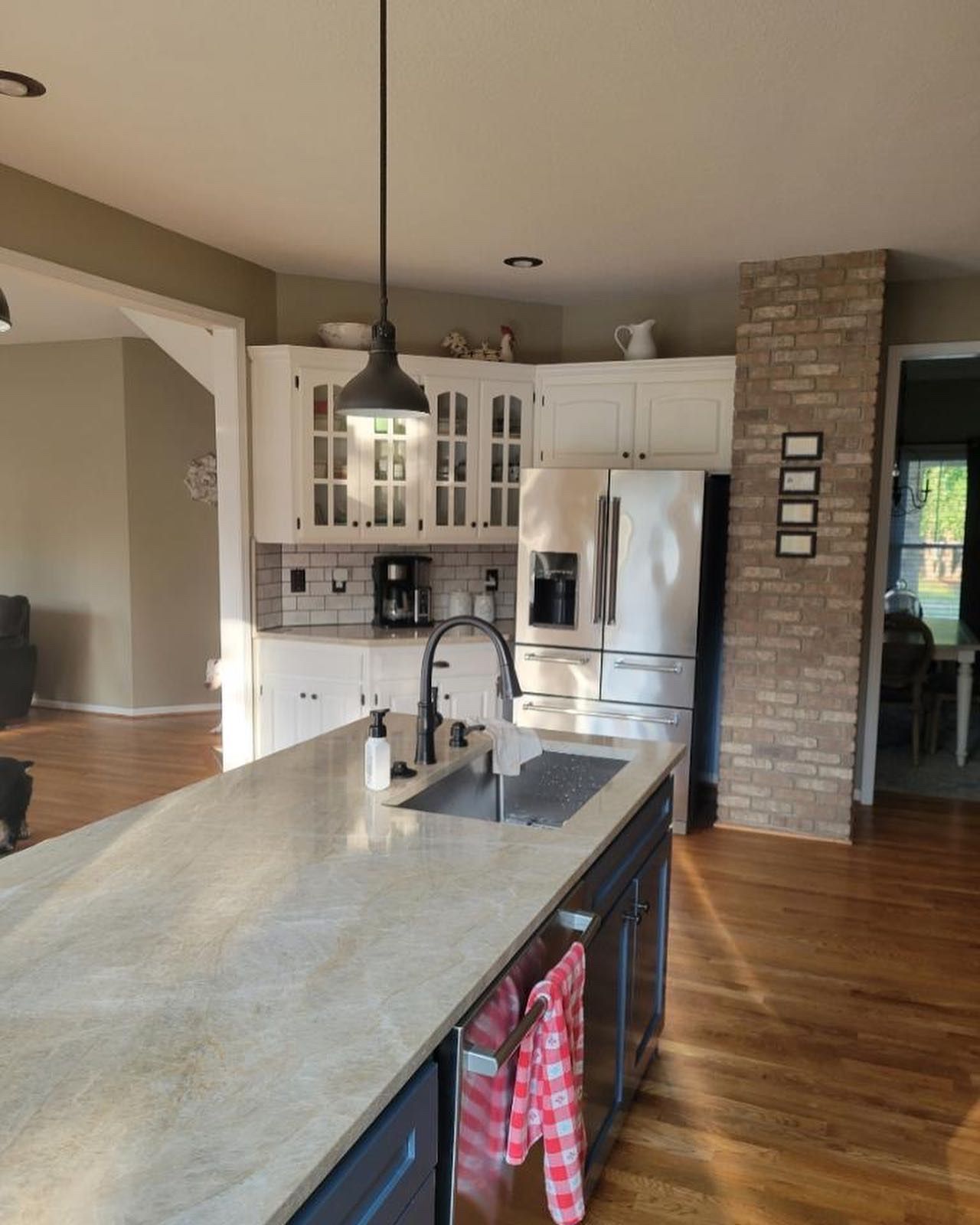 A modern kitchen featuring a dark blue island with a stone countertop, white cabinets, stainless appliances, and brick wall.