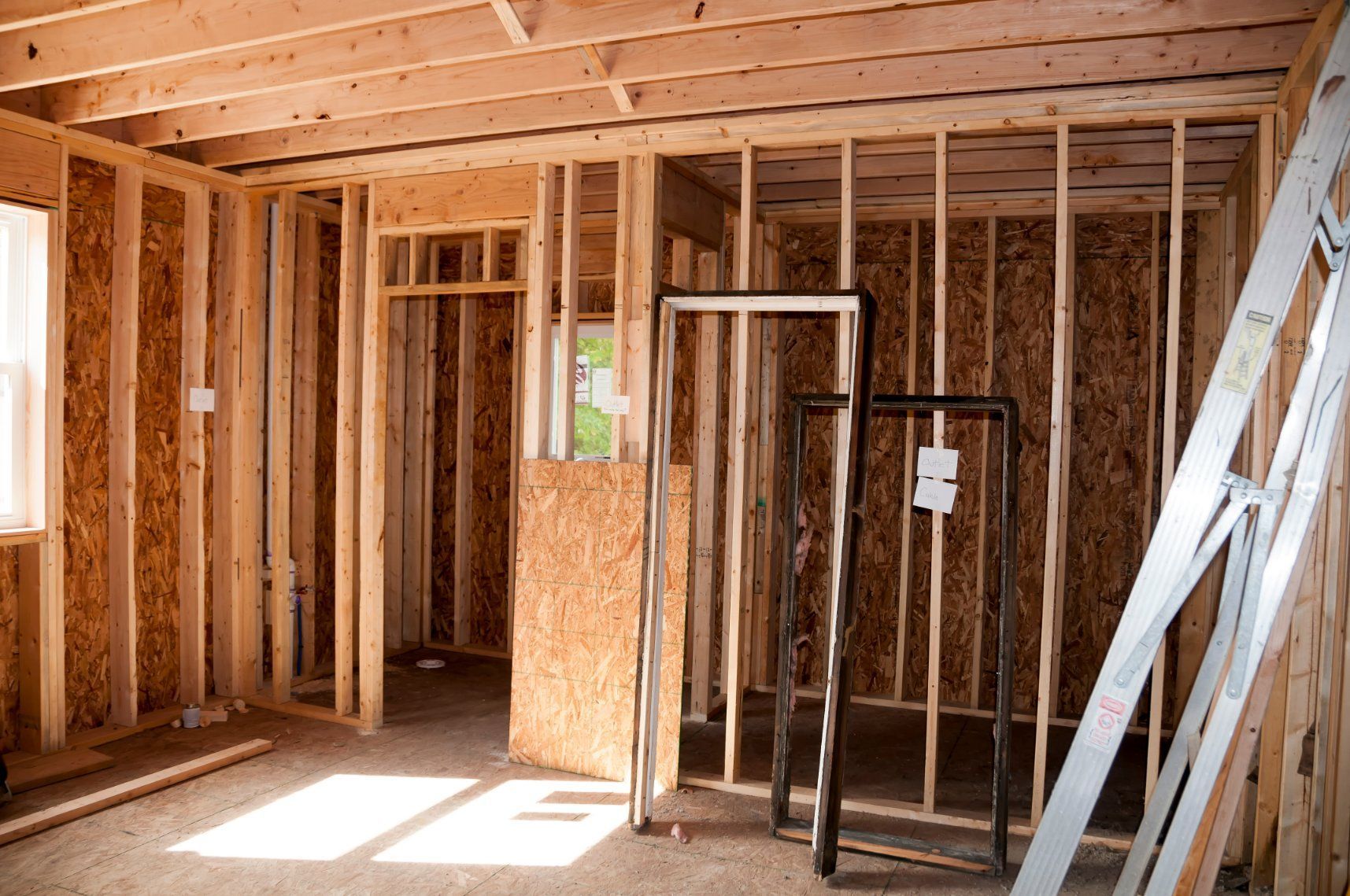 Interior of a room under construction; wood framing and exposed wall supports; door frames in the foreground.